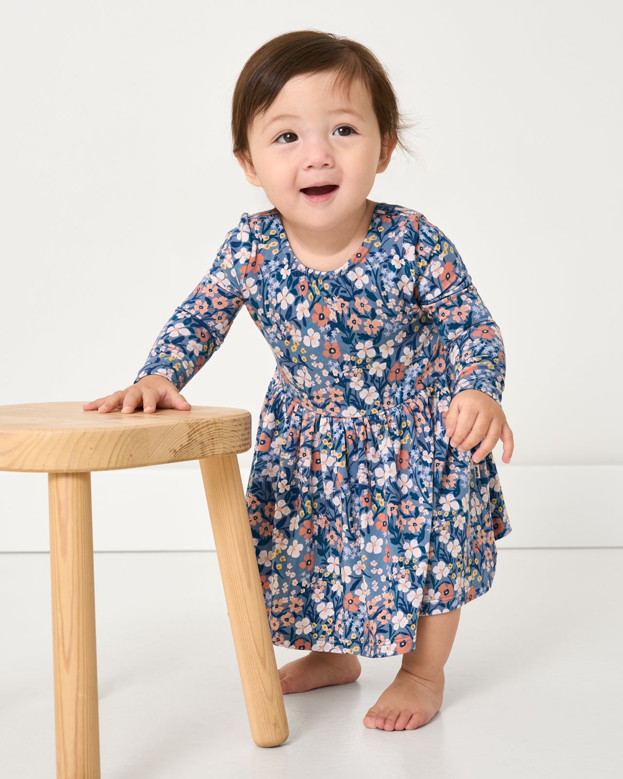 Standing baby wearing the Petite Petals Bow Back Skater Dress with Bodysuit