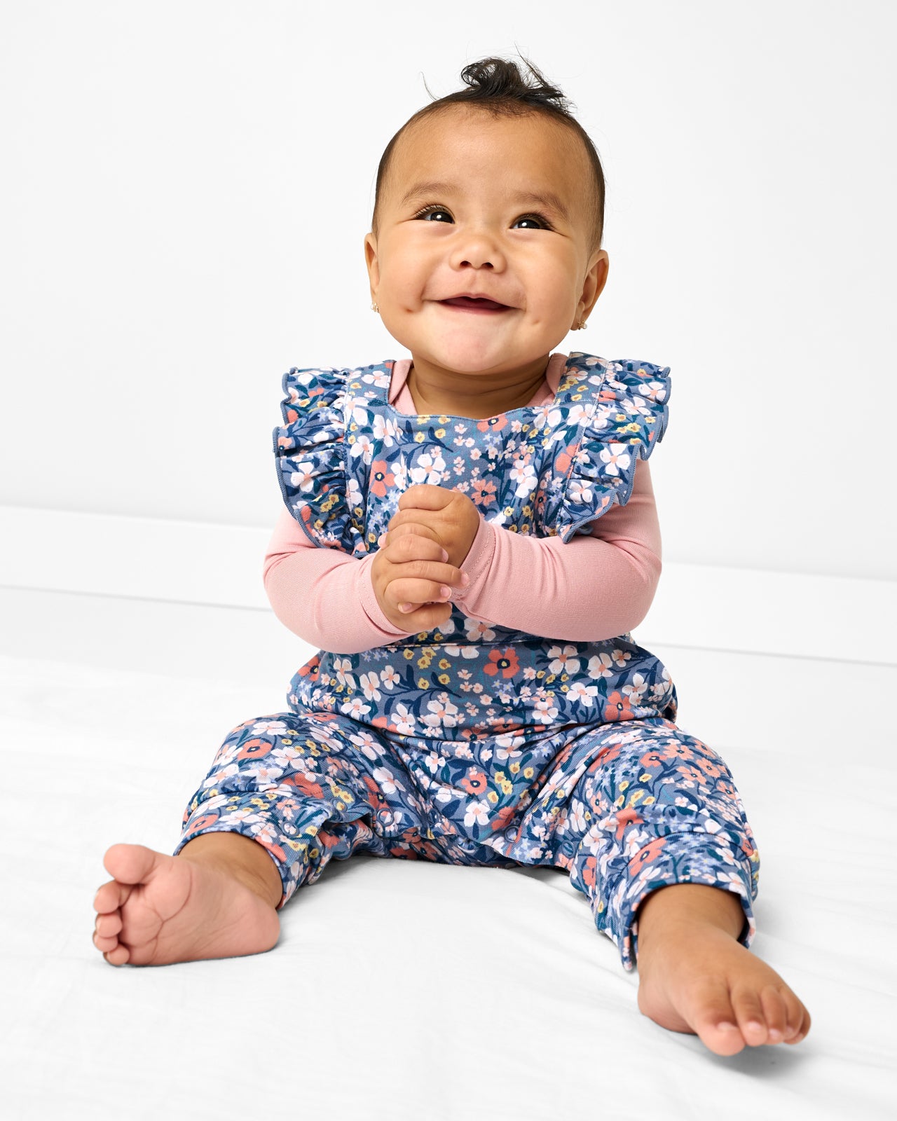 Sitting baby wearing the Petite Petals Ruffle Overall