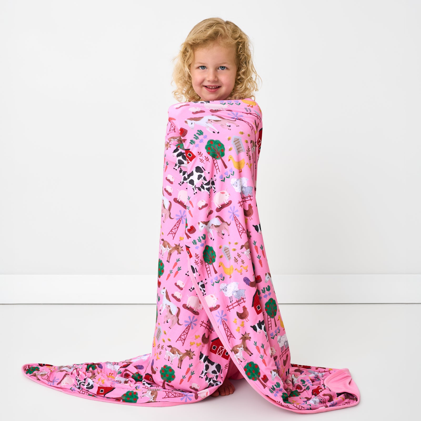 Standing child wrapped in the Pink Farm Fam Large Cloud Blanket®