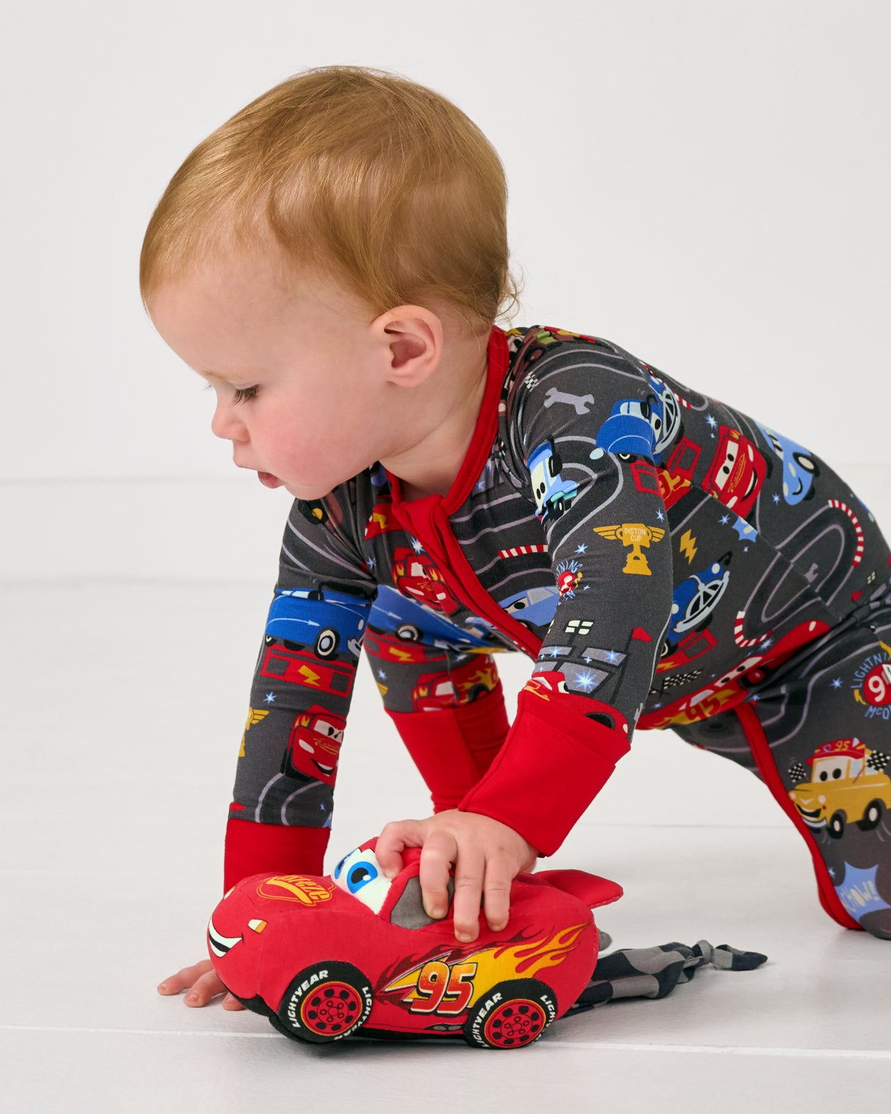Baby wearing the Disney & Pixar Piston Cup Zippy playing with the race car lovey
