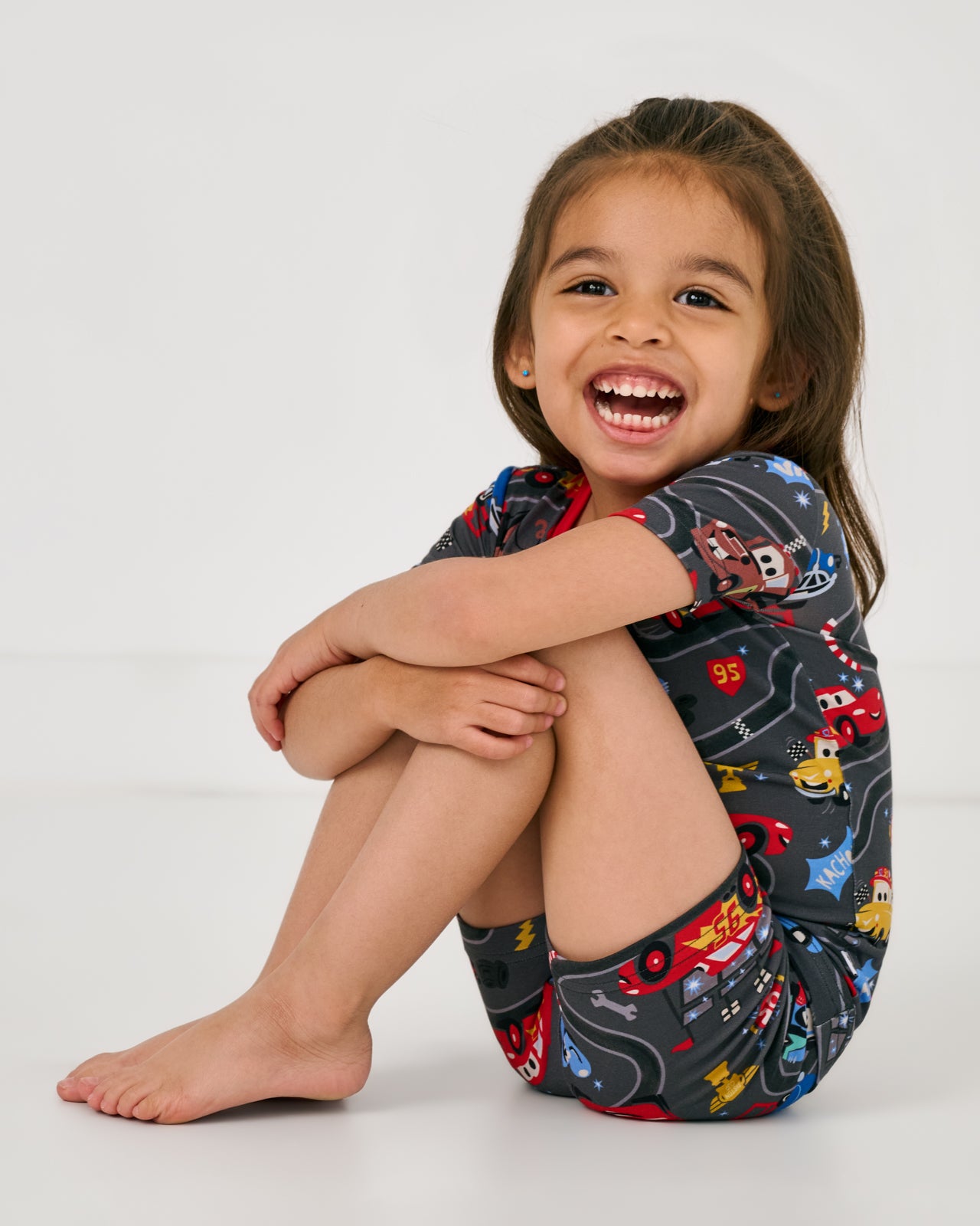Sitting girl wearing the Disney & Pixar Piston Cup Two-Piece Short Sleeve & Shorts Pajama Set