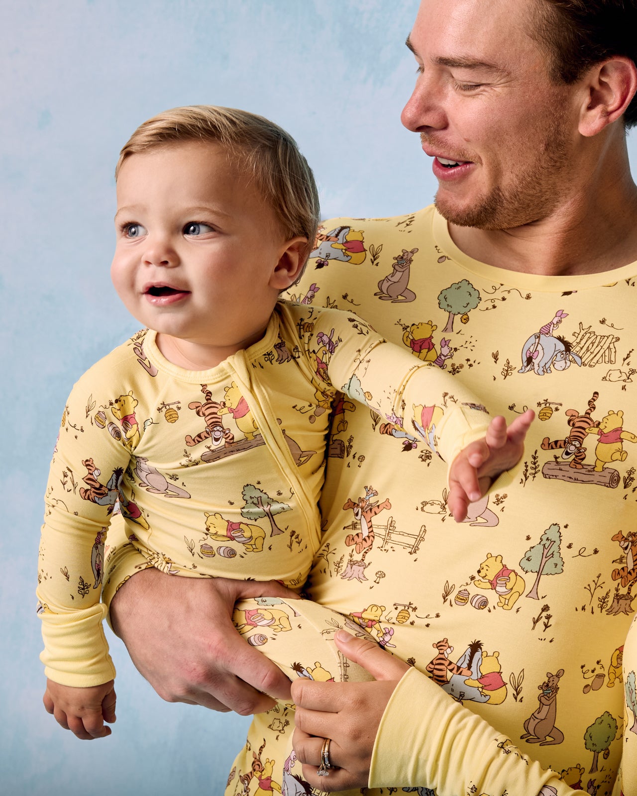 Father and child wearing matching Disney Playtime With Pooh pajamas on a blue background