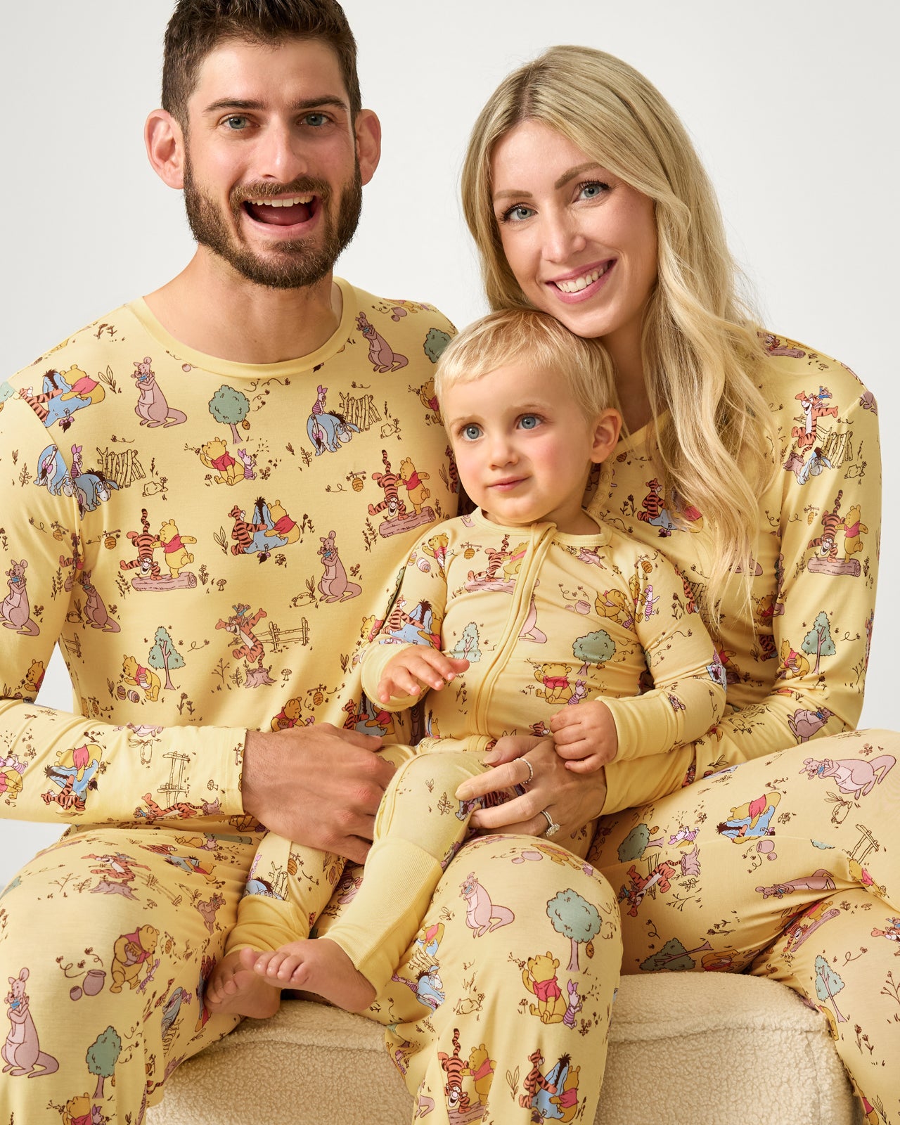 Family of three wearing matching Disney Playtime With Pooh pajamas