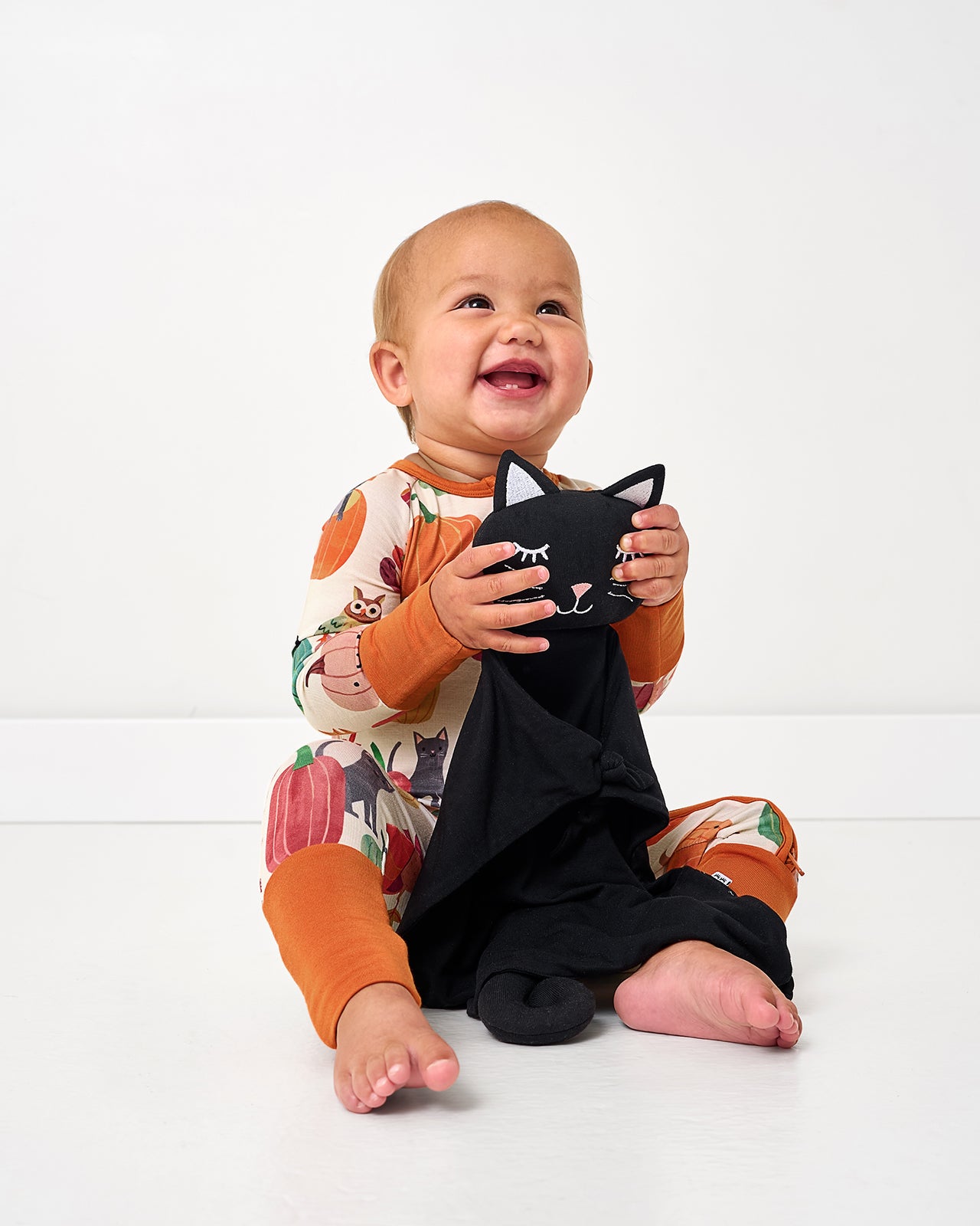 Sitting baby wearing the Pumpkin Pals Zippy holding a cat lovey