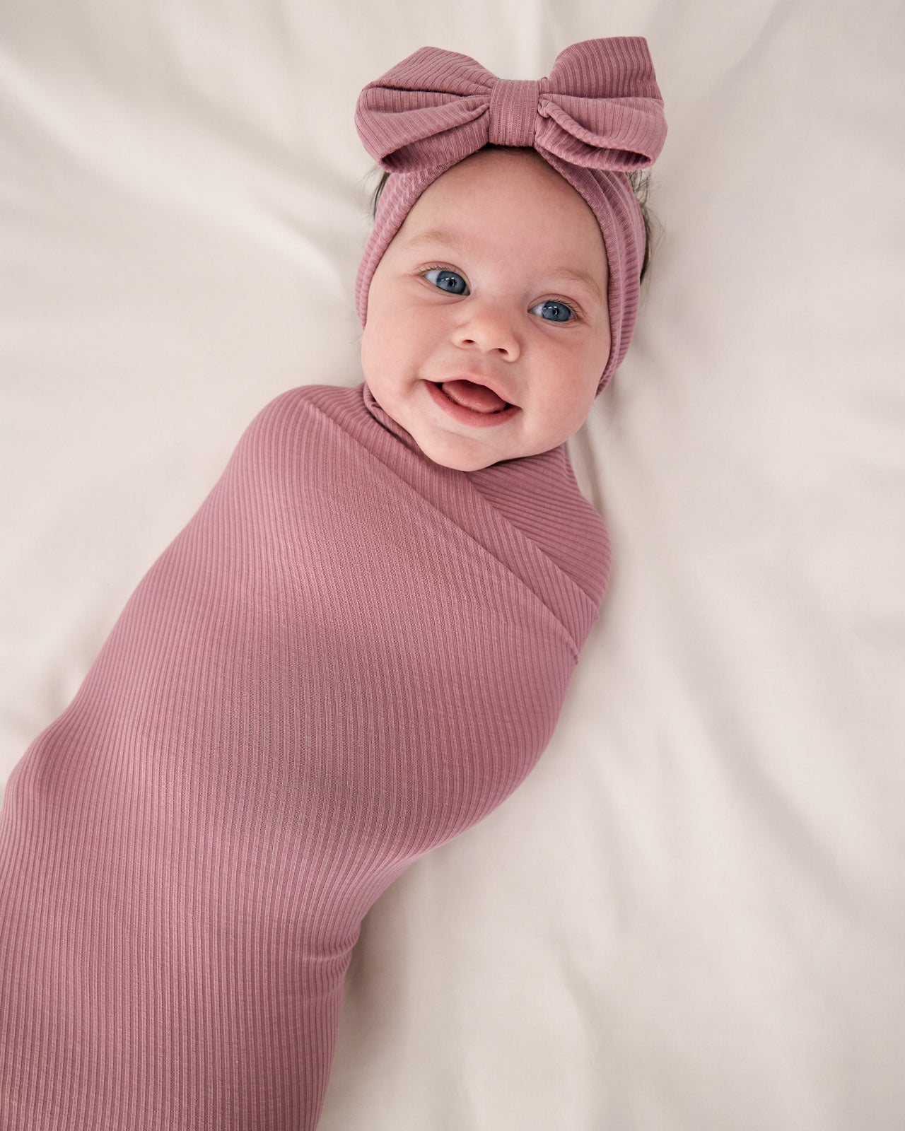 Aerial view of baby swaddled in the Rosewood Ribbed Swaddle & Luxe Bow Headband Set