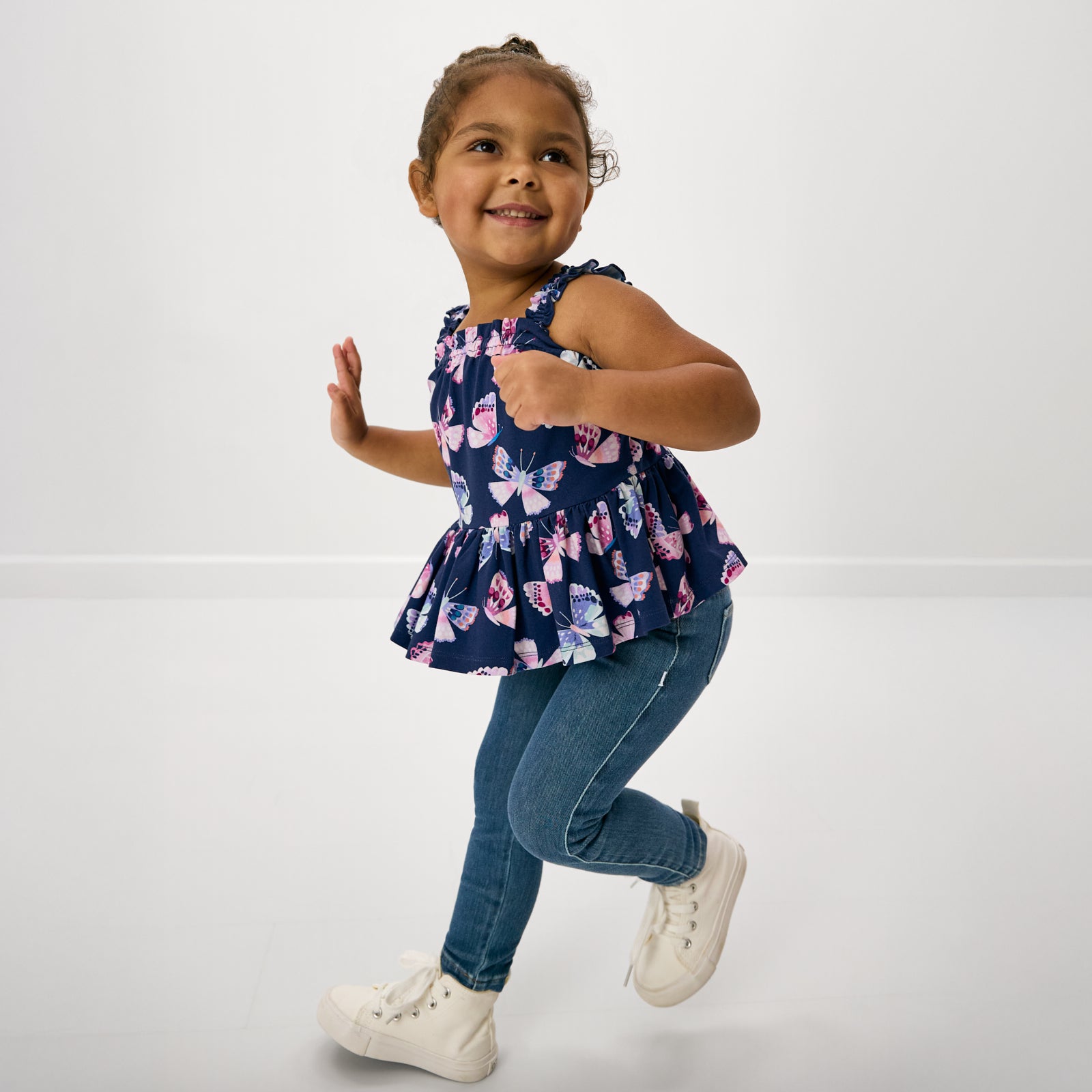 Child in motion wearing the Royal Butterflies Peplum Flutter Tank with denim jeggings