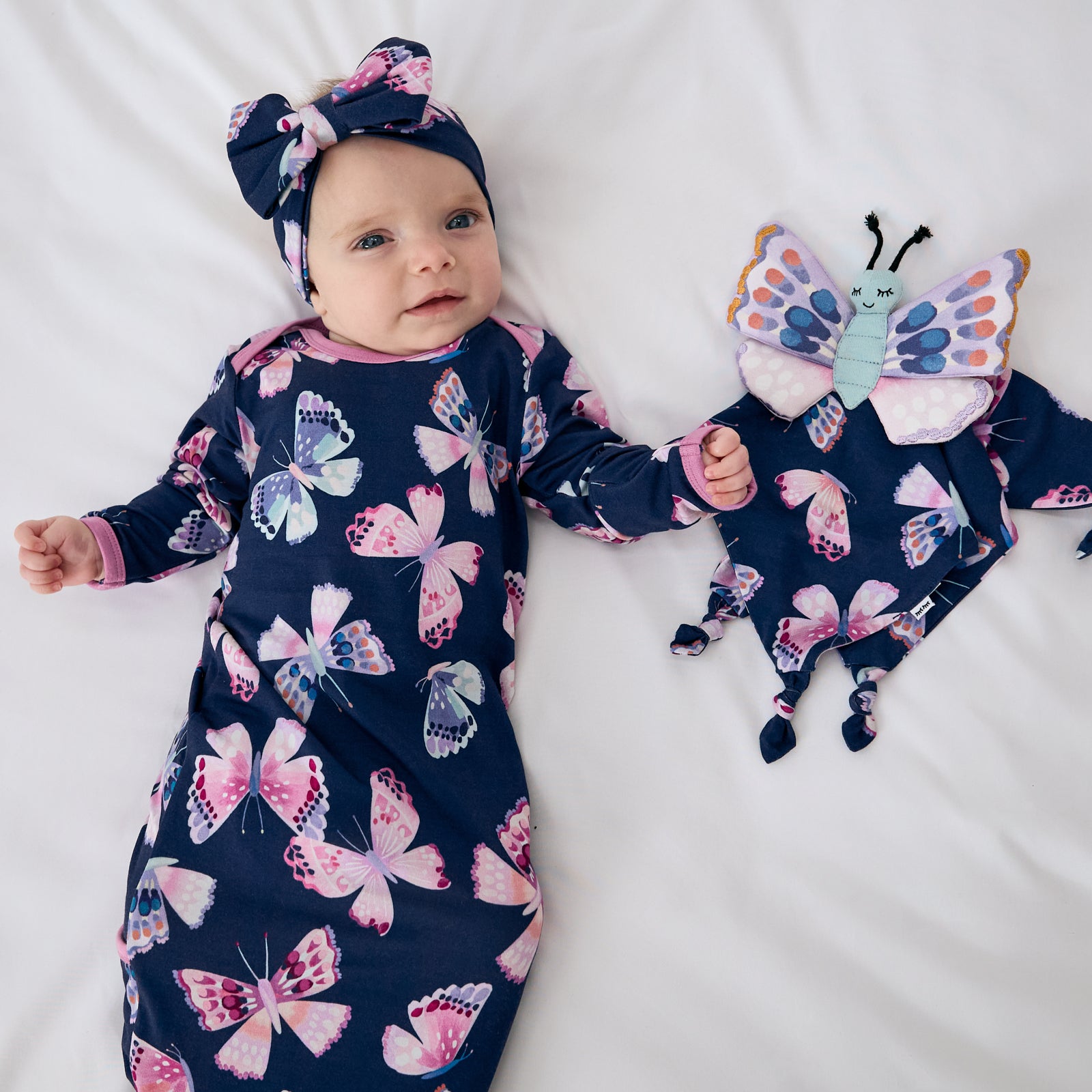 Baby wearing the Royal Butterflies Infant Gown laying with the butterfly lovey