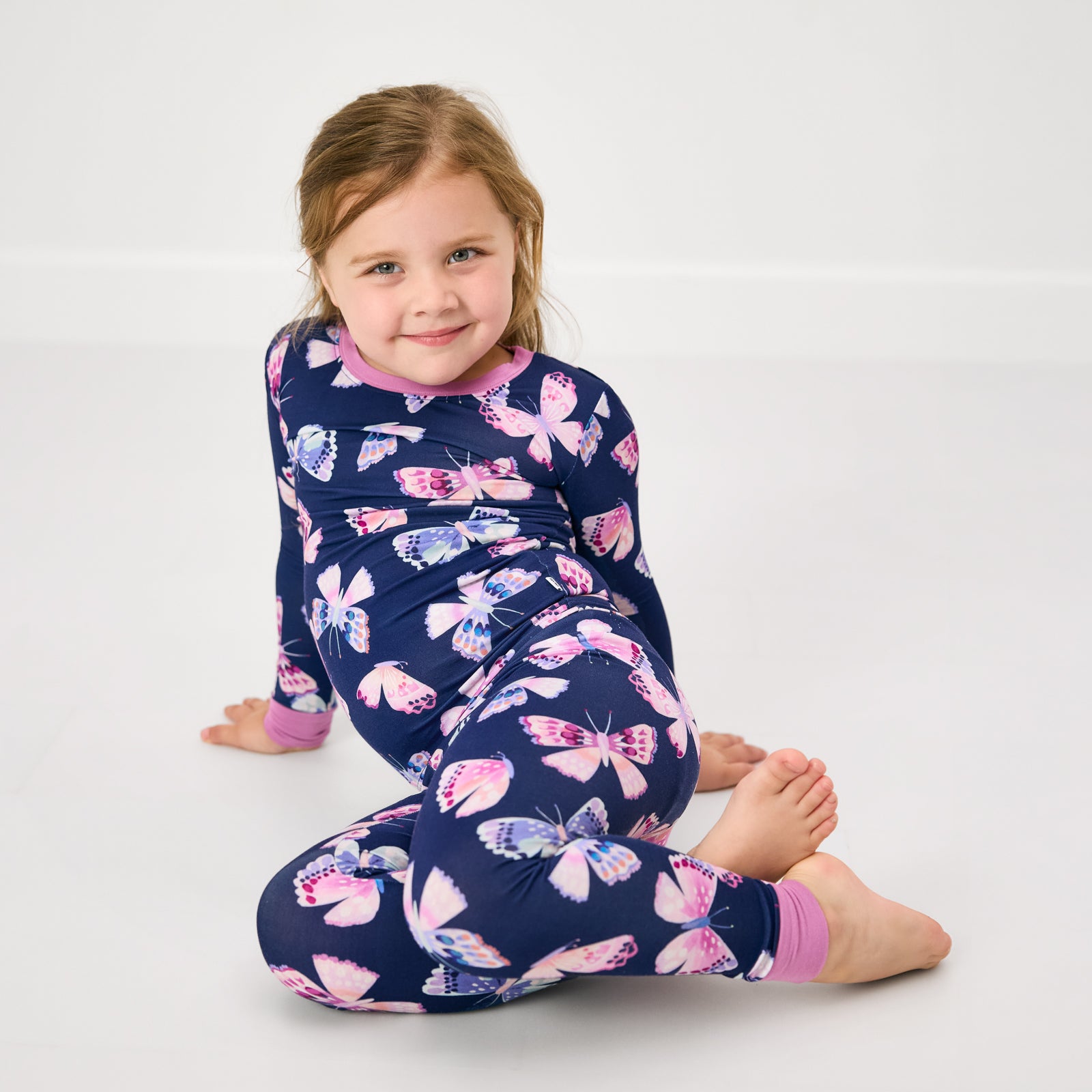 Sitting girl wearing the Royal Butterflies Two-Piece Bamboo Kids Pajama Set