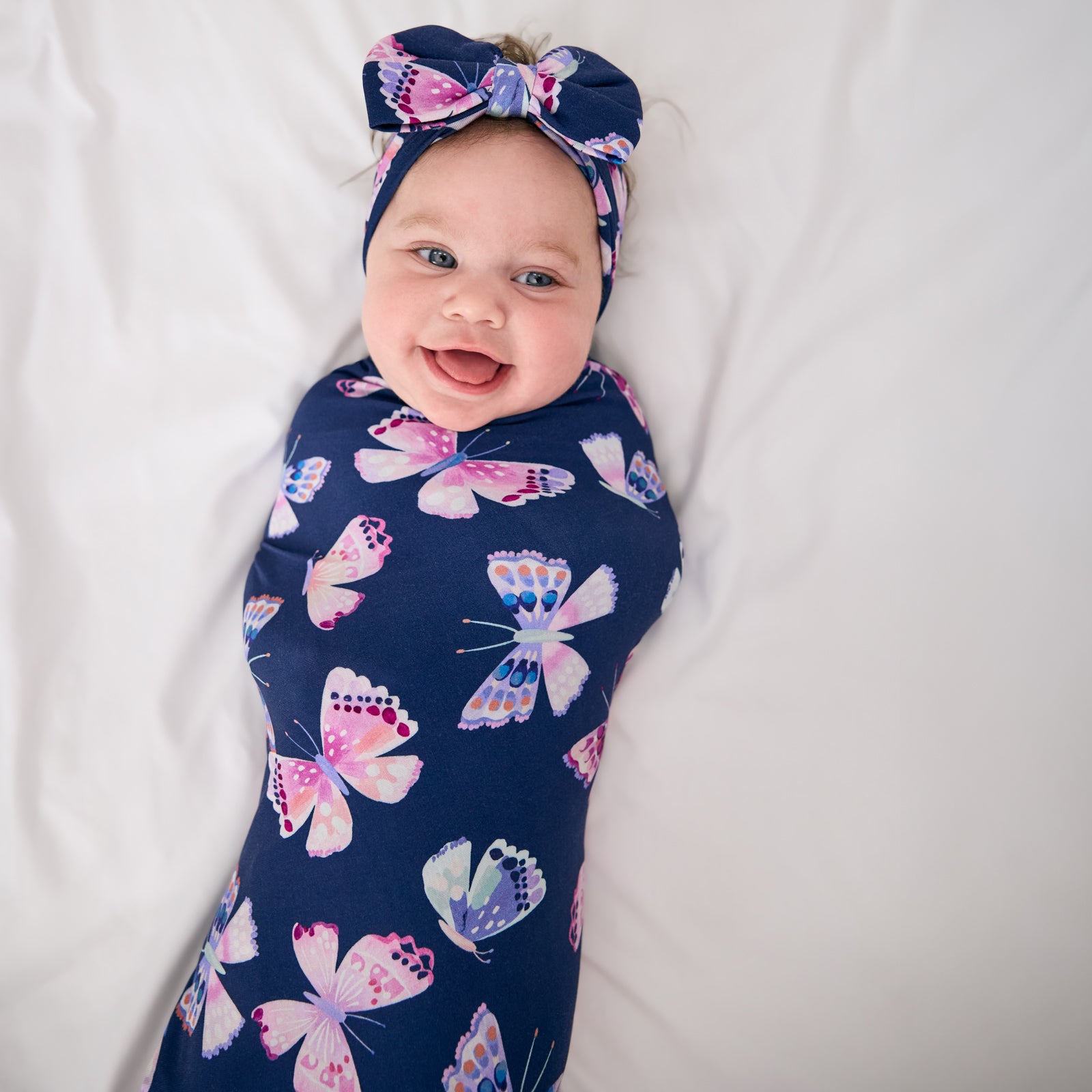 Aerial view of alternate baby wearing the Royal Butterflies Swaddle & Luxe Bow Headband Set
