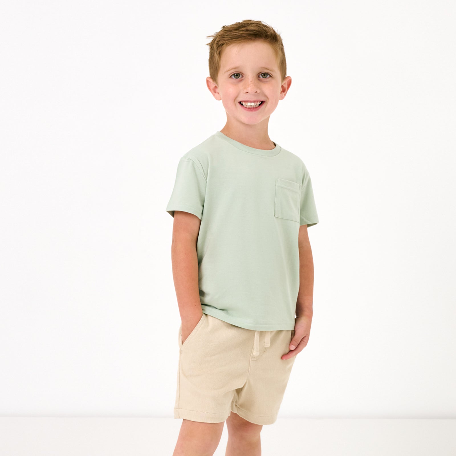 Standing child wearing the Sage Mist Relaxed Pocket Tee with light khaki shorts