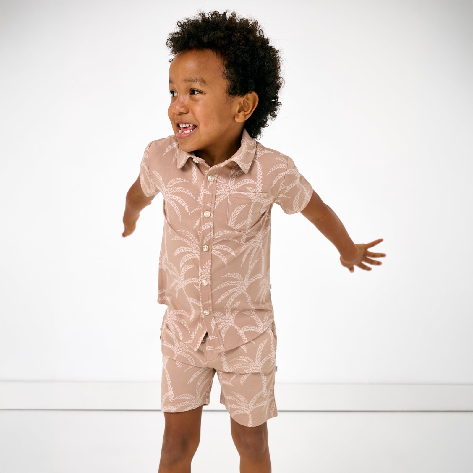Jumping child wearing the Sandy Palms Button Down Polo with matching shorts