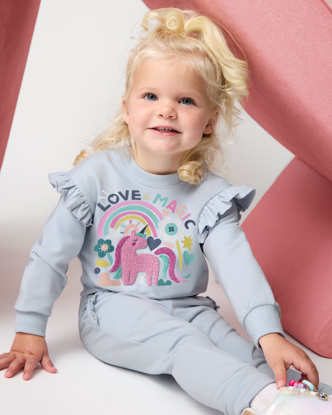 Sitting girl wearing the Unicorn Ruffle Crewneck and coordinating joggers