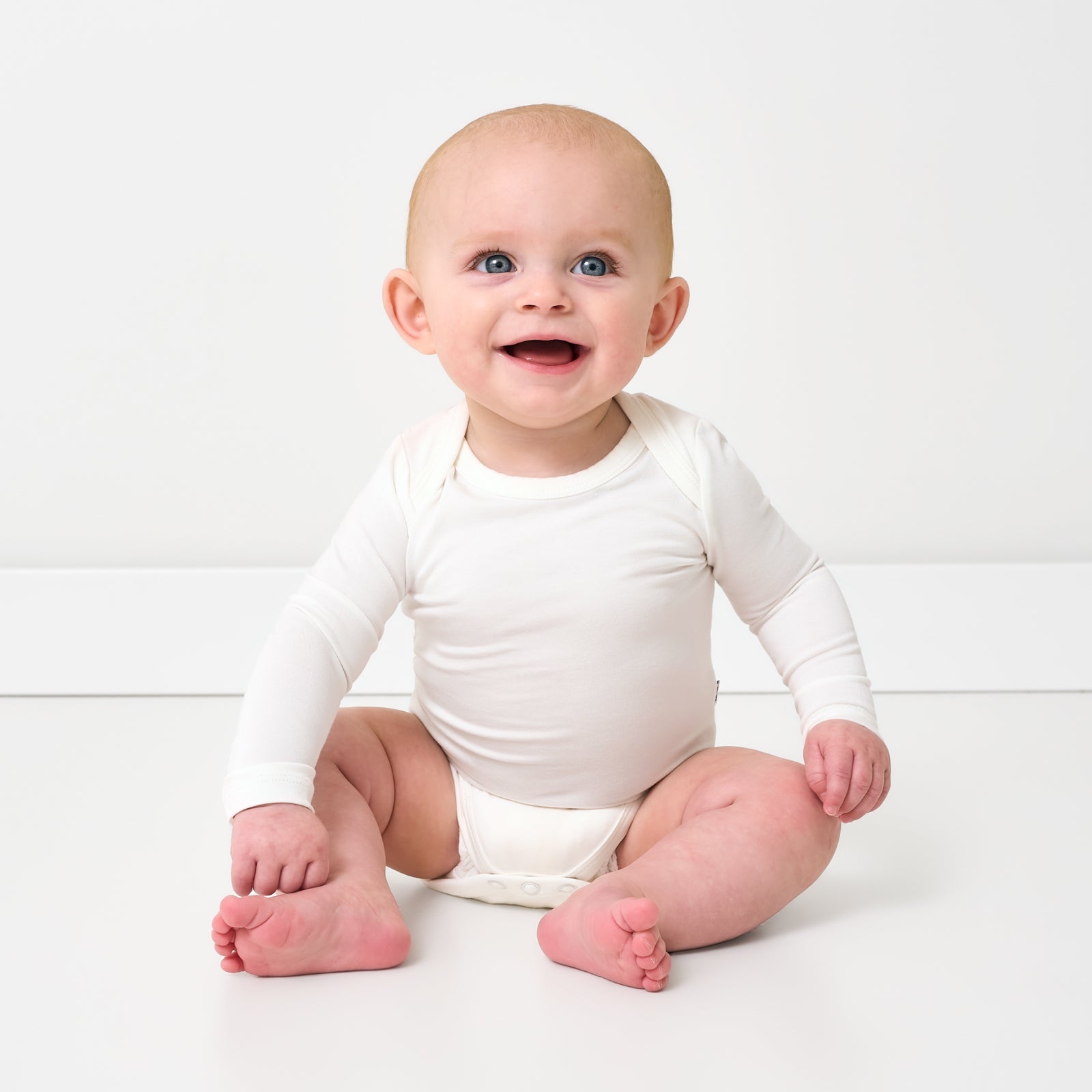 Sitting baby wearing the Soft White Long Sleeve Bodysuit
