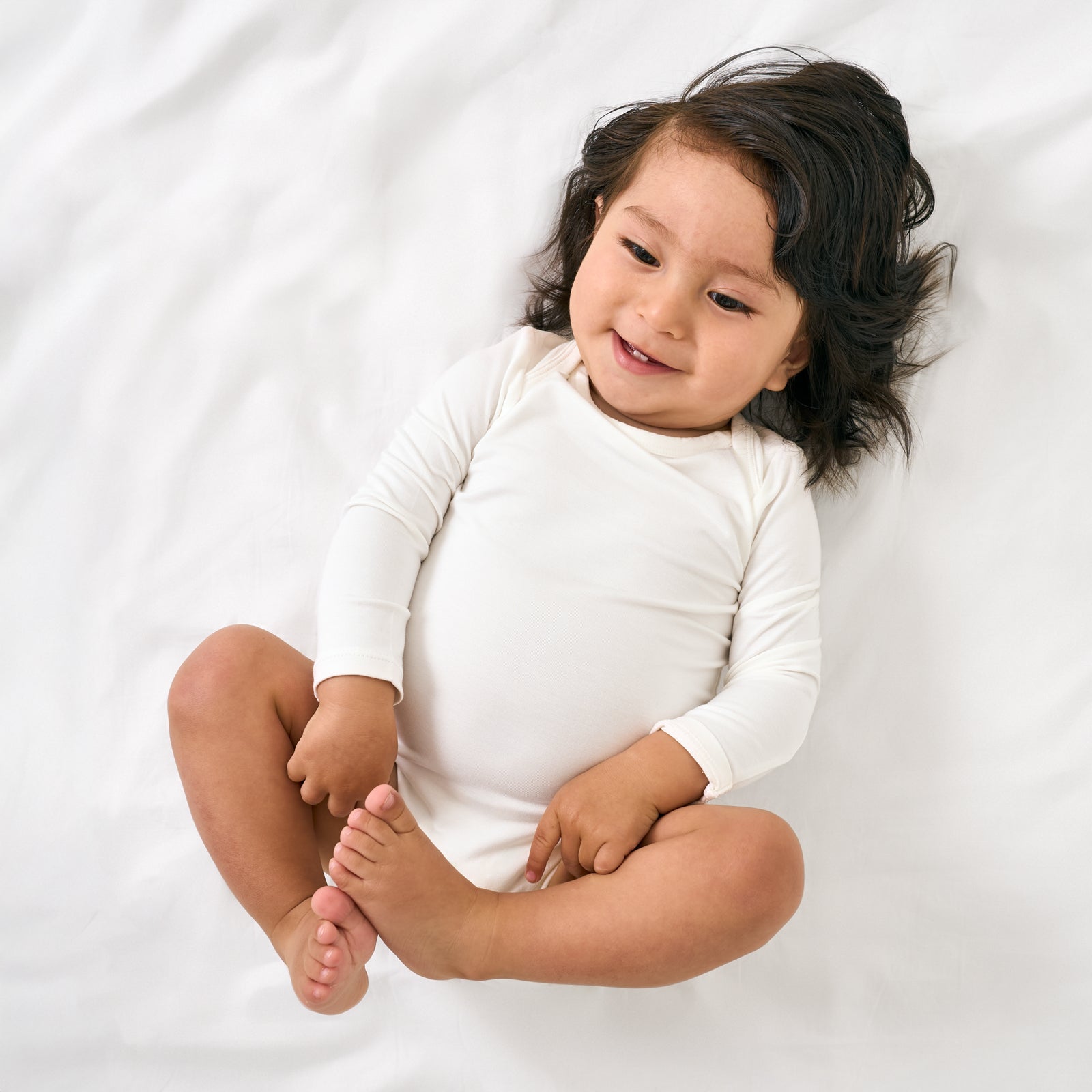 Aerial view of baby wearing the Soft White Long Sleeve Bodysuit