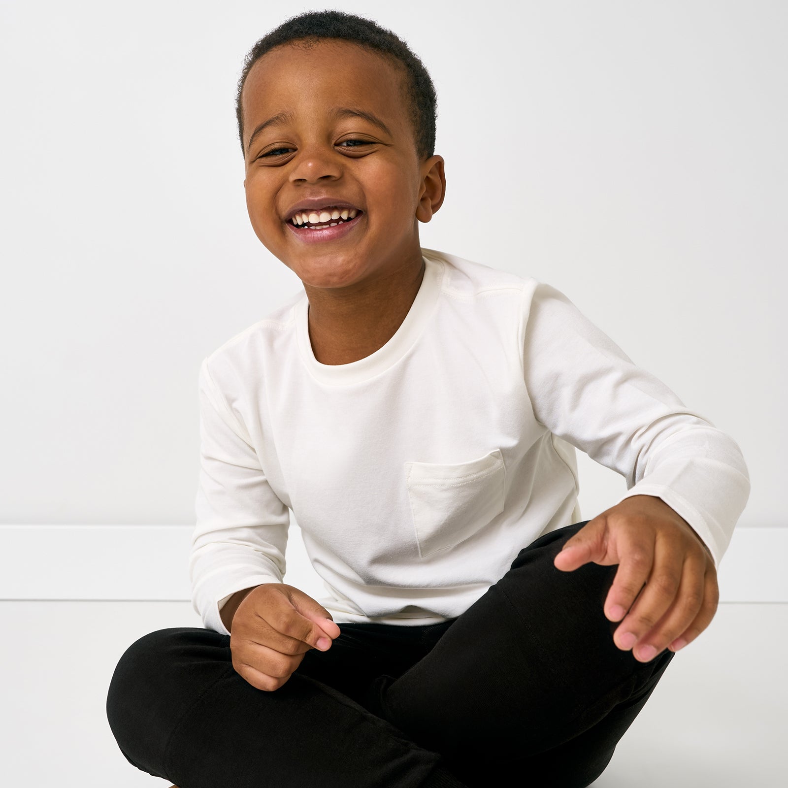 Sitting child wearing the Soft White Long Sleeve Relaxed Pocket Tee