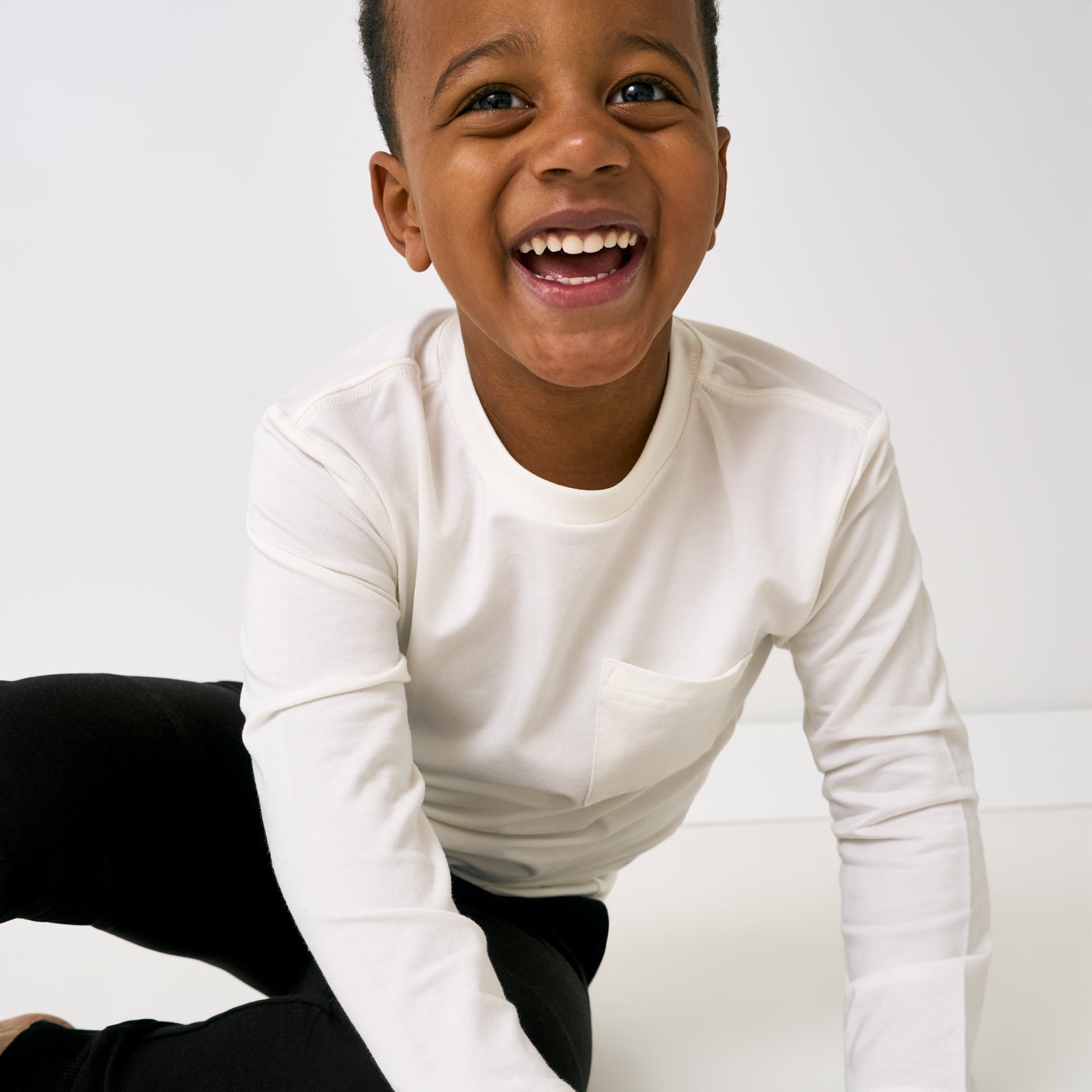 Close up of sitting child wearing the Soft White Long Sleeve Relaxed Pocket Tee