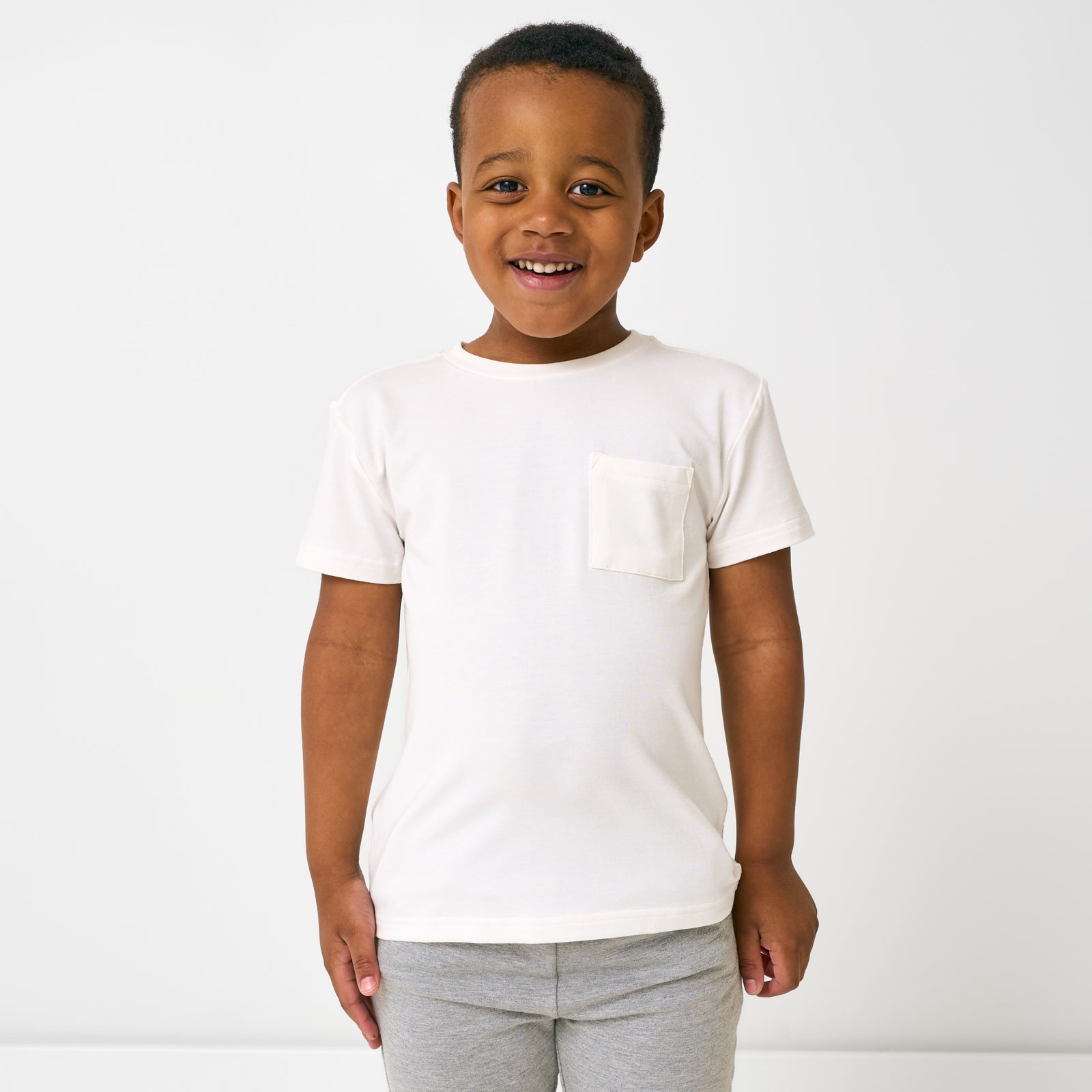 Standing child wearing the Soft White Short Sleeve Relaxed Pocket Tee with gray shorts