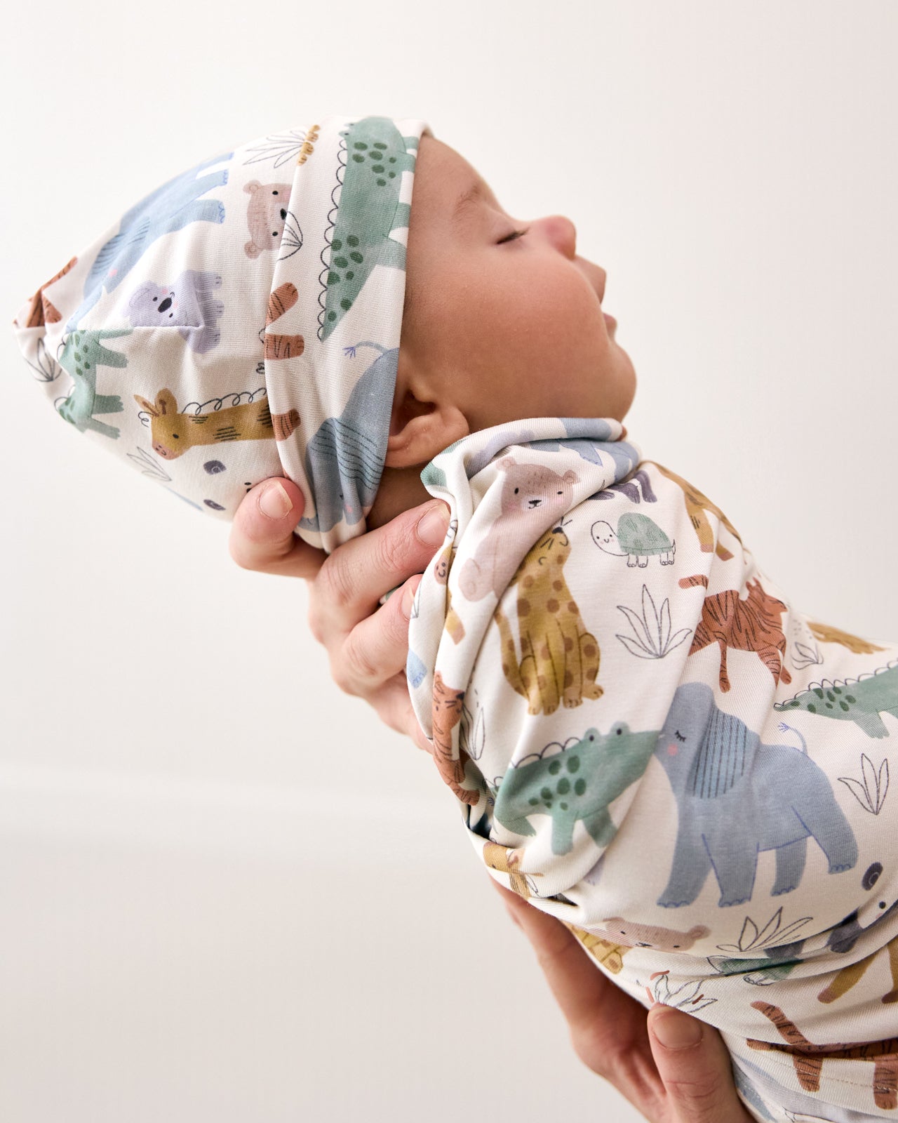 Baby in the Sweet Safari Swaddle & Infant Beanie Set being held