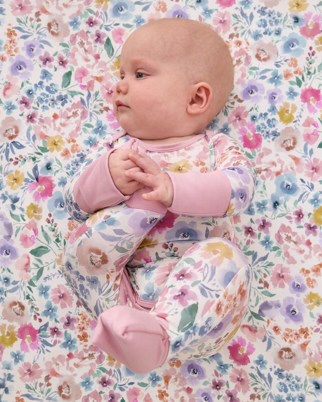 Aerial view of newborn wearing the Tiny Blooms Crescent Zippy on a matching floral crib sheet