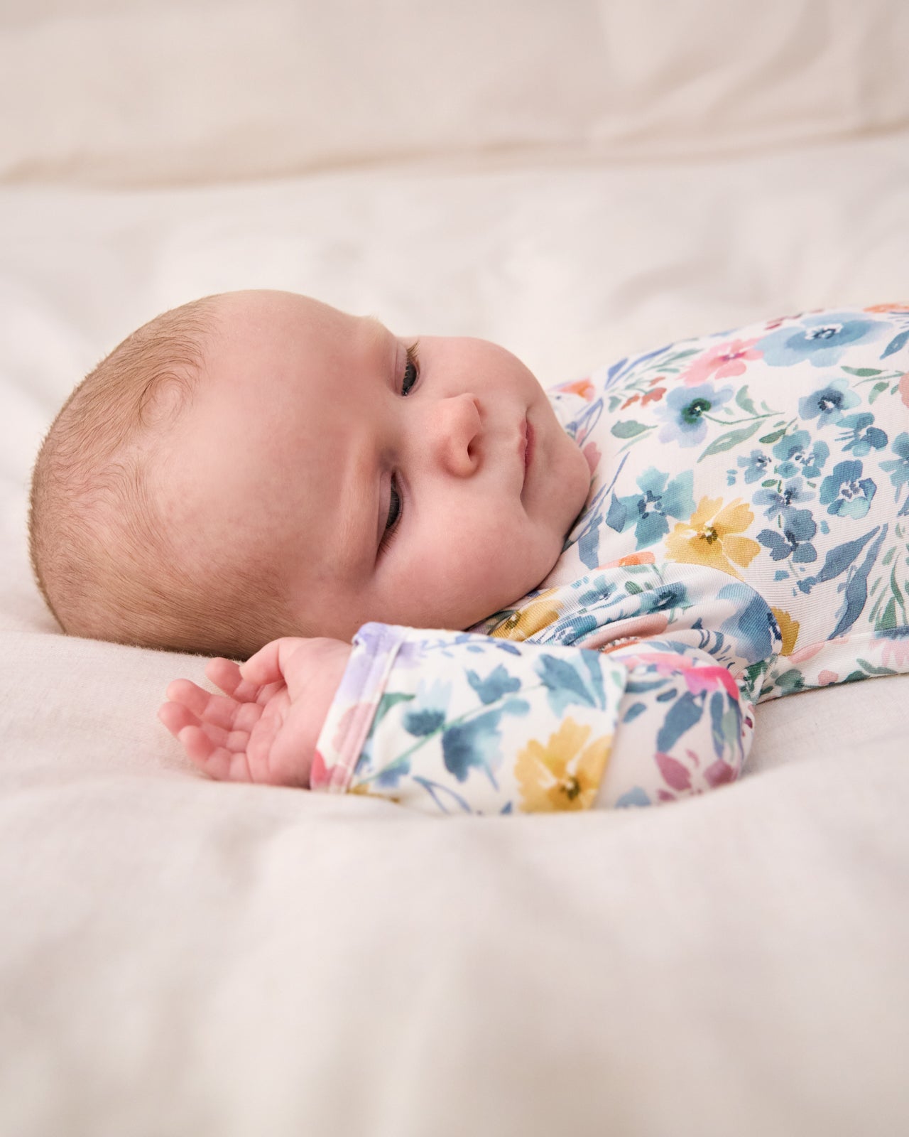 Baby laying on a white blanket wearing the Tiny Blooms Infant Gown
