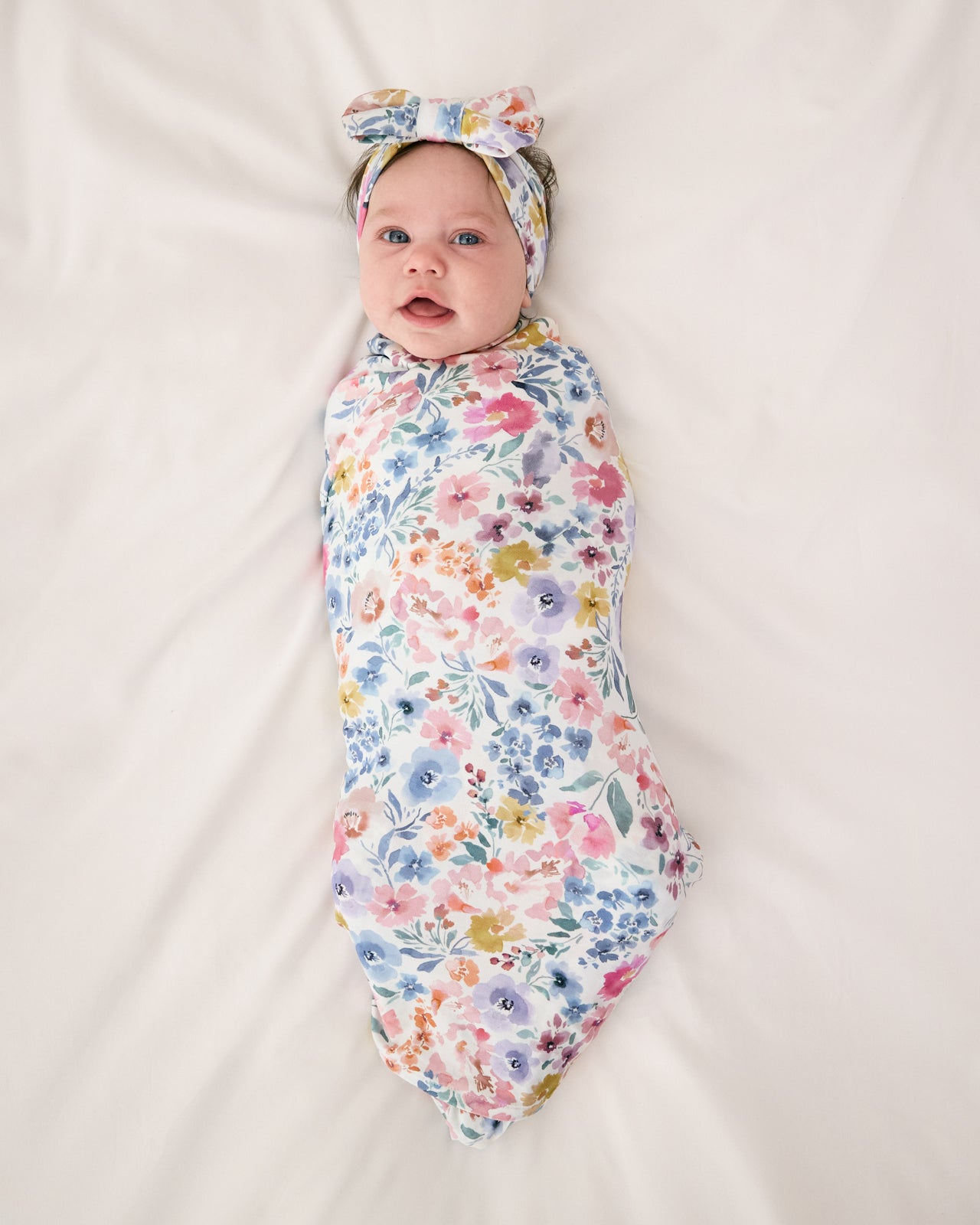 Aerial view of baby wearing the Tiny Blooms Swaddle & Luxe Bow Headband Set