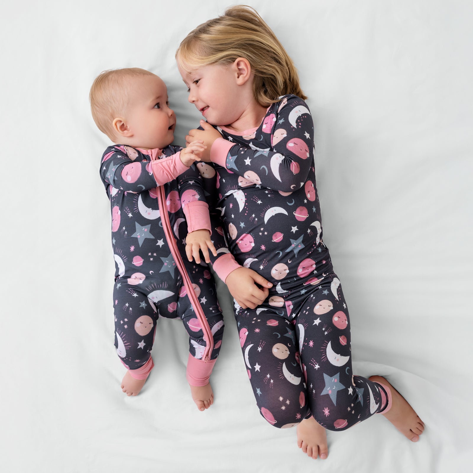 Two siblings wearing matching Pink To the Moon & Back bamboo pajamas