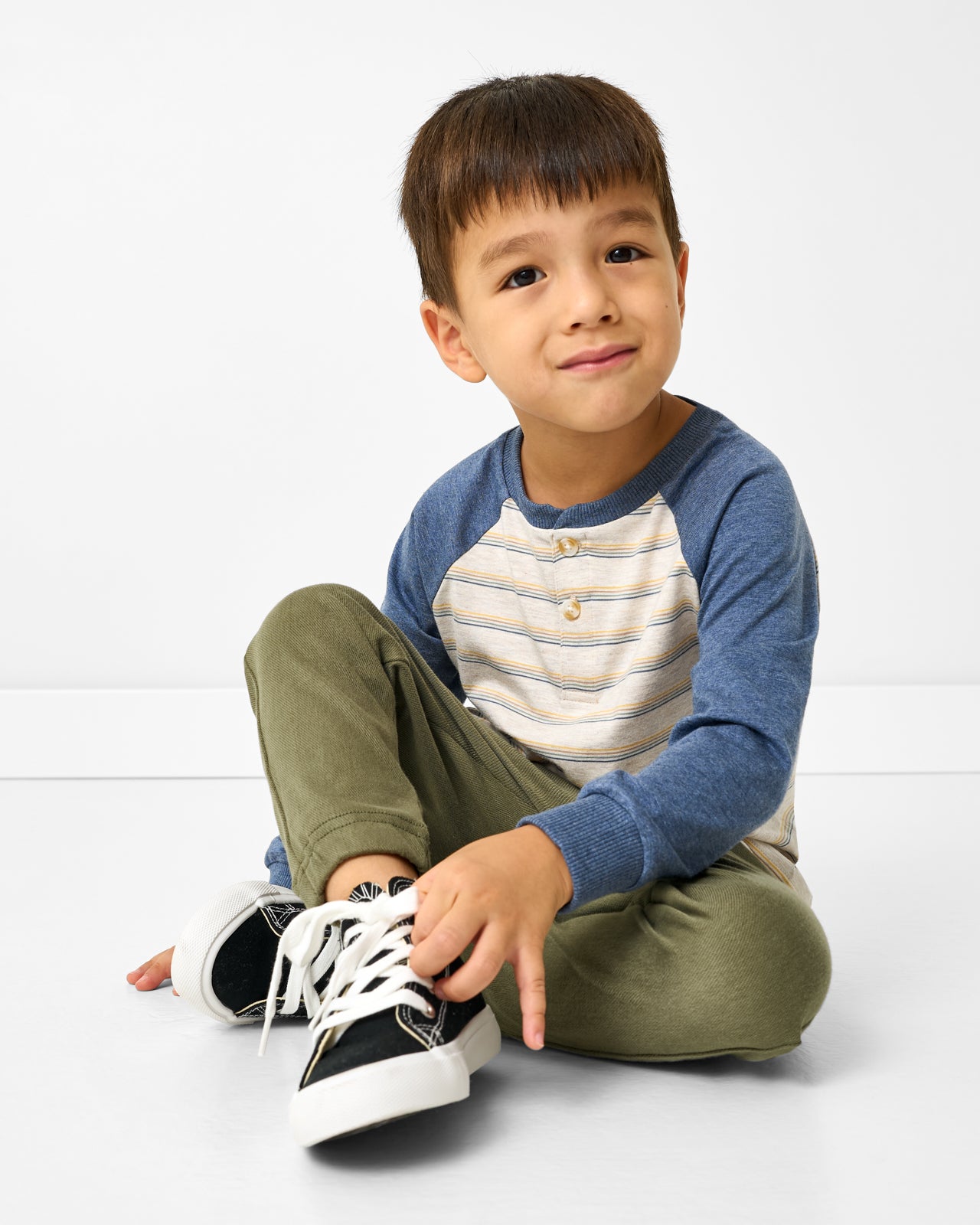 Sitting boy wearing the Vintage Navy Heather Stripe Raglan Henley Tee with green pants