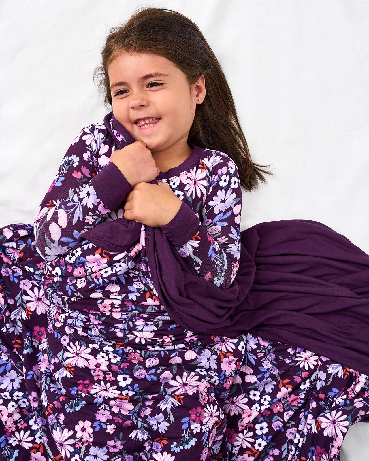 Girl laying on a white bed wrapped in the Violet Meadow Large Cloud Blanket®