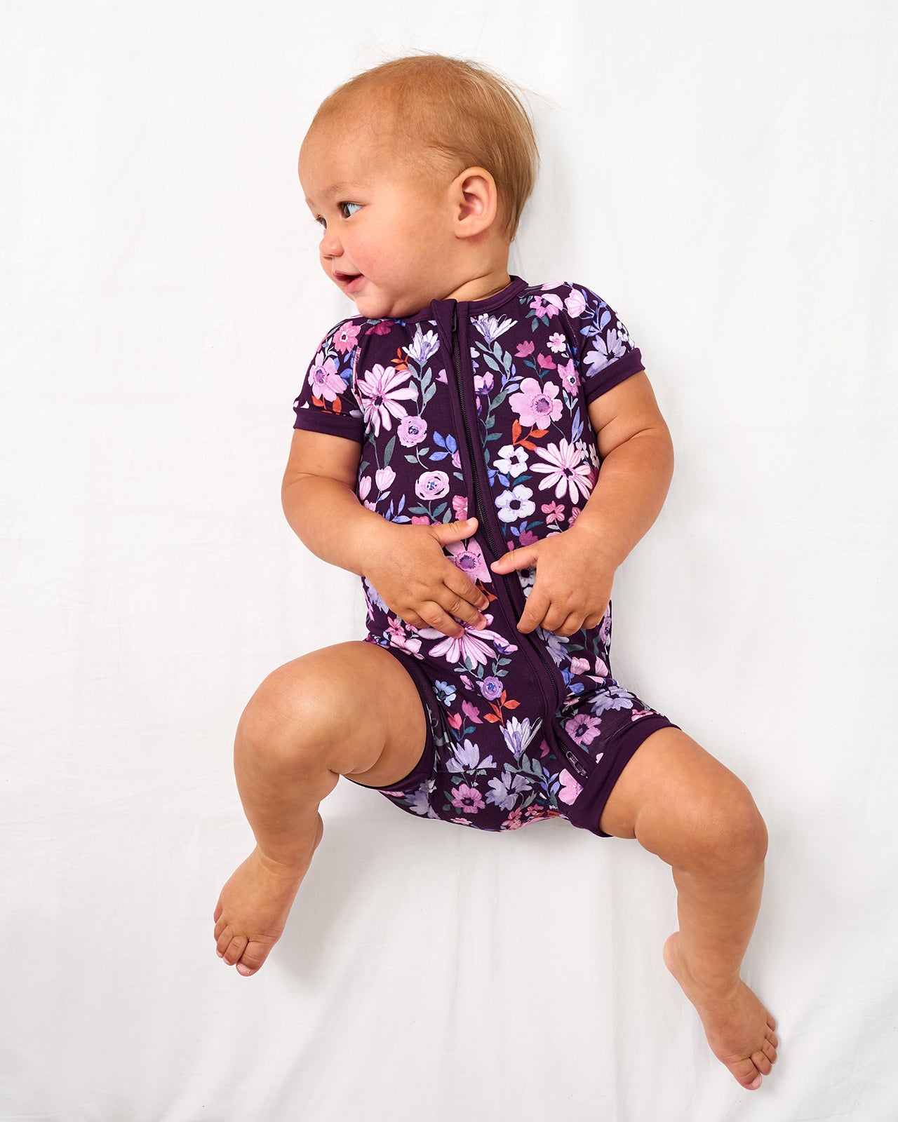 Baby wearing the Violet Meadow Shorty Zippy on a white bed