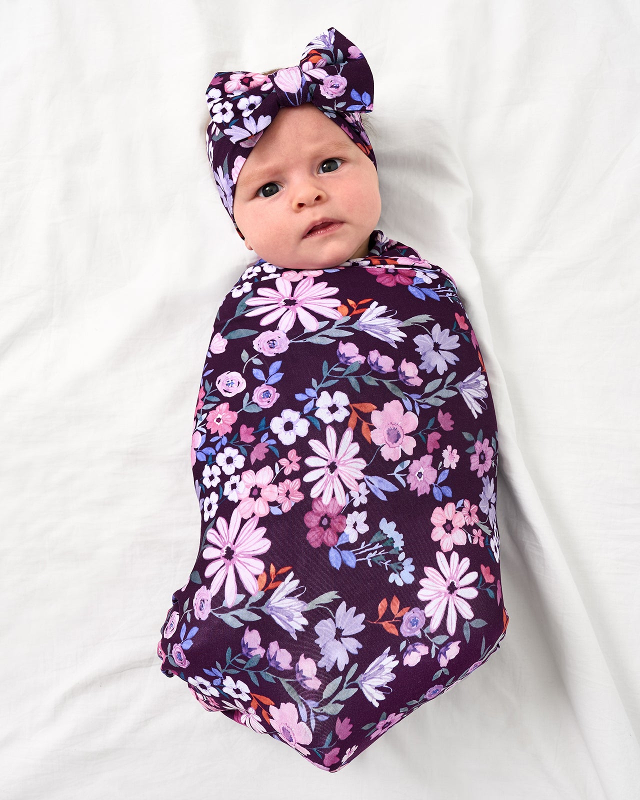 Aerial view of baby wearing the Violet Meadow Swaddle & Luxe Bow Headband Set