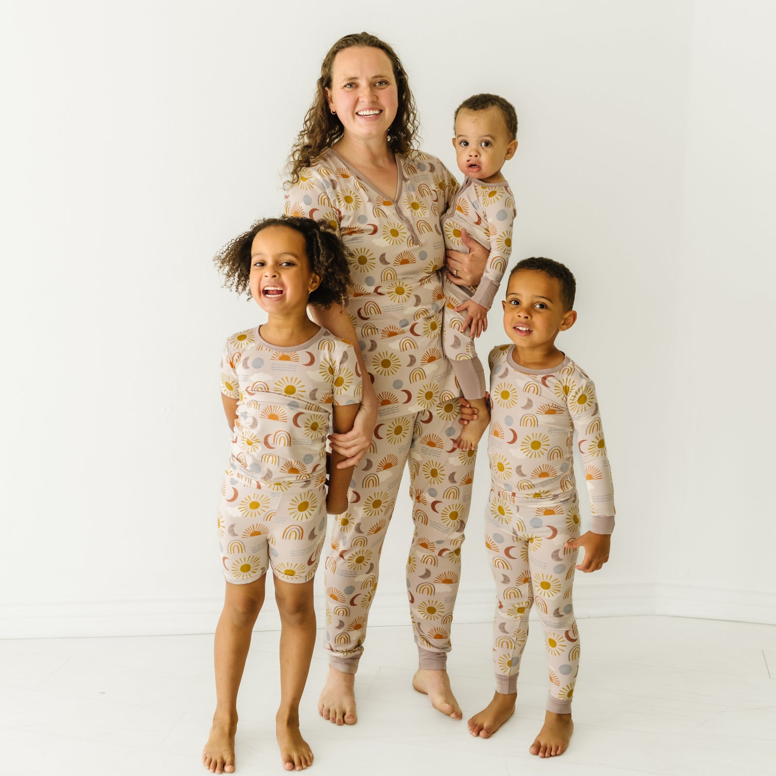 Mother and her three kids wearing matching Desert Sunrise pjs. Mom is wearing women's Desert Sunrise women's pajama top and matching women's pajama pants. Children are wearing Desert Sunrise pjs in two piece and zippy styles