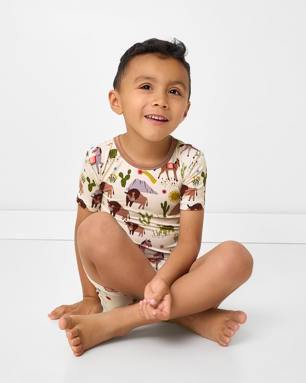 Sitting boy wearing the Wild Frontier Two-Piece Short Sleeve & Shorts Pajama Set