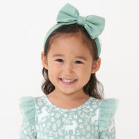 Close up image of a child wearing an Aqua Mist luxe bow headband paired with a Unicorn Garden flutter dress