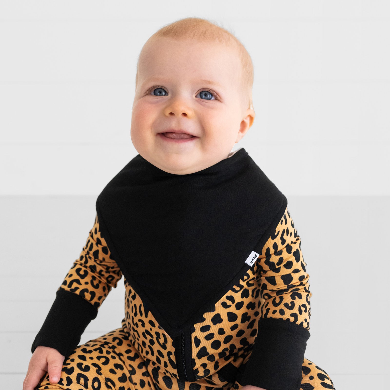 Smiling child wearing a Black Bandana Bib over a Classic Leopard Zippy