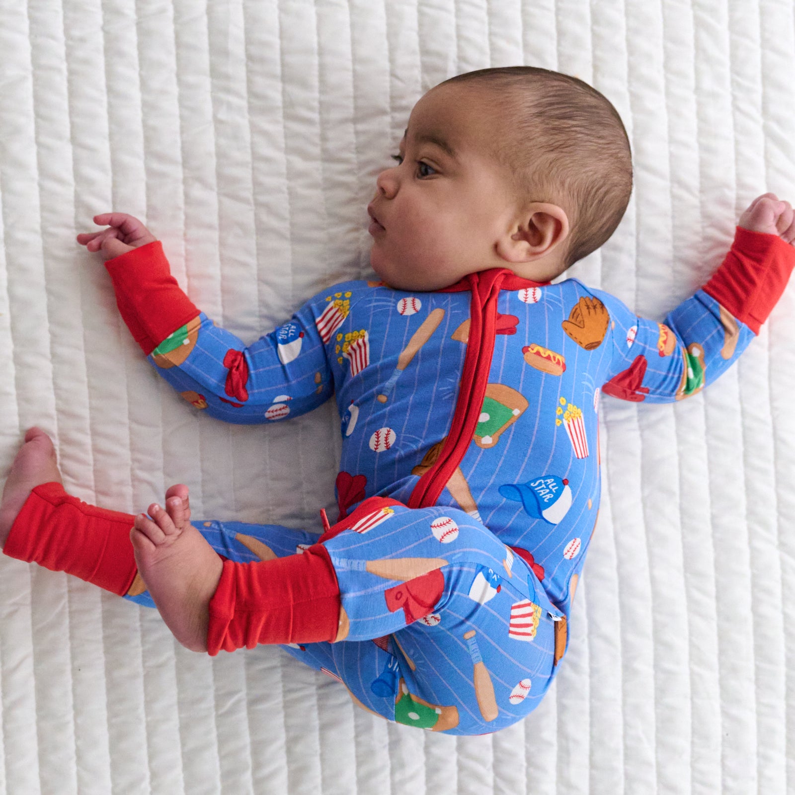 Baby laying down and looking to the left wearing a Blue All Stars bamboo zippy
