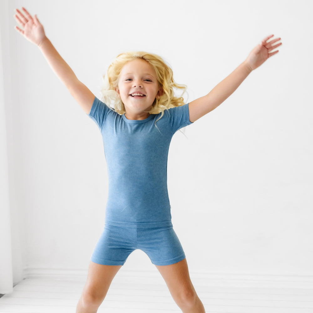 Child jumping wearing Heather Blue Ribbed two piece short sleeve and shorts pajama set