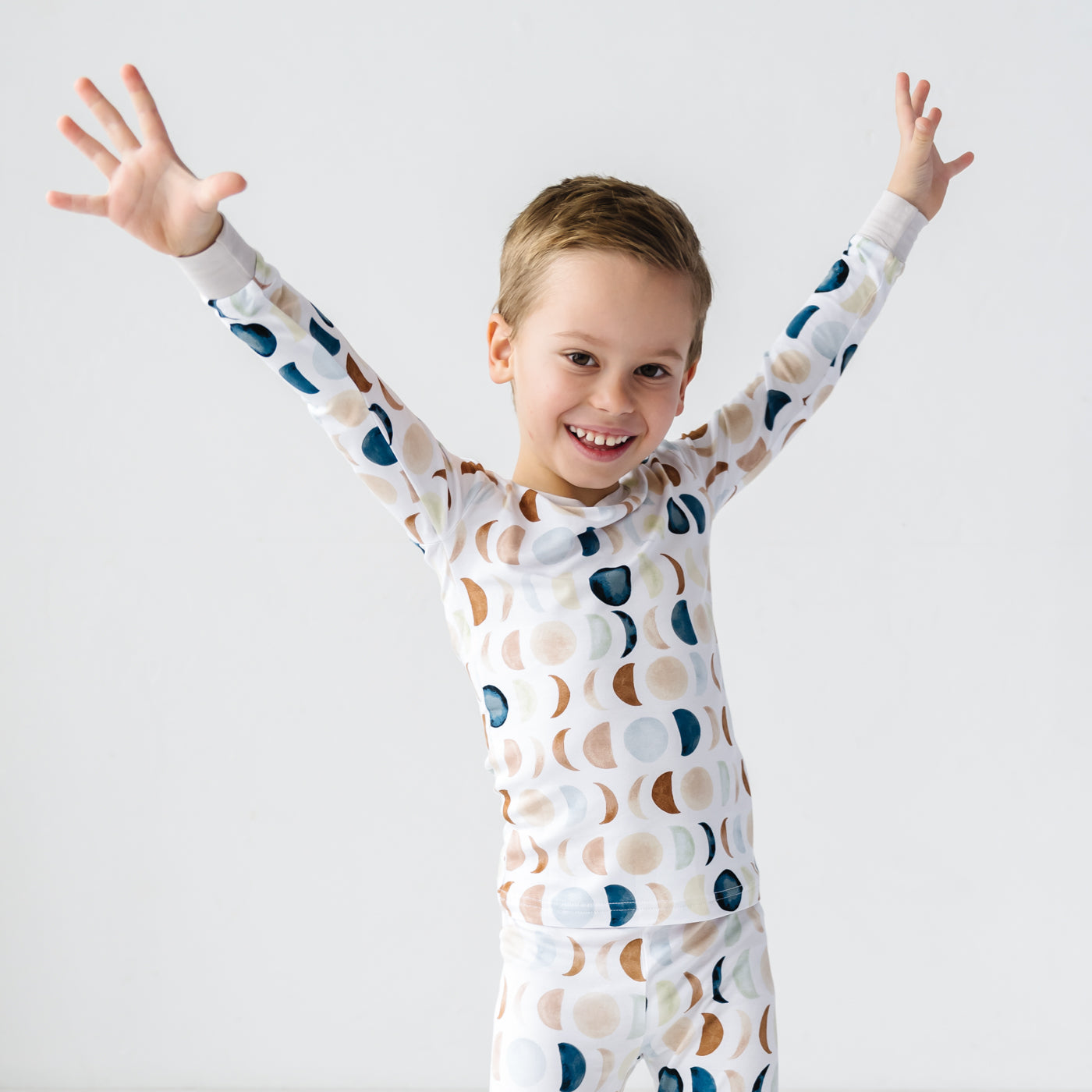 Image of a toddler in long sleeve top and pajama pants set in Luna Neutral print. This print features phases of the moon in the sweetest shades of creams, tans, and navy watercolor in an all over repeat pattern.