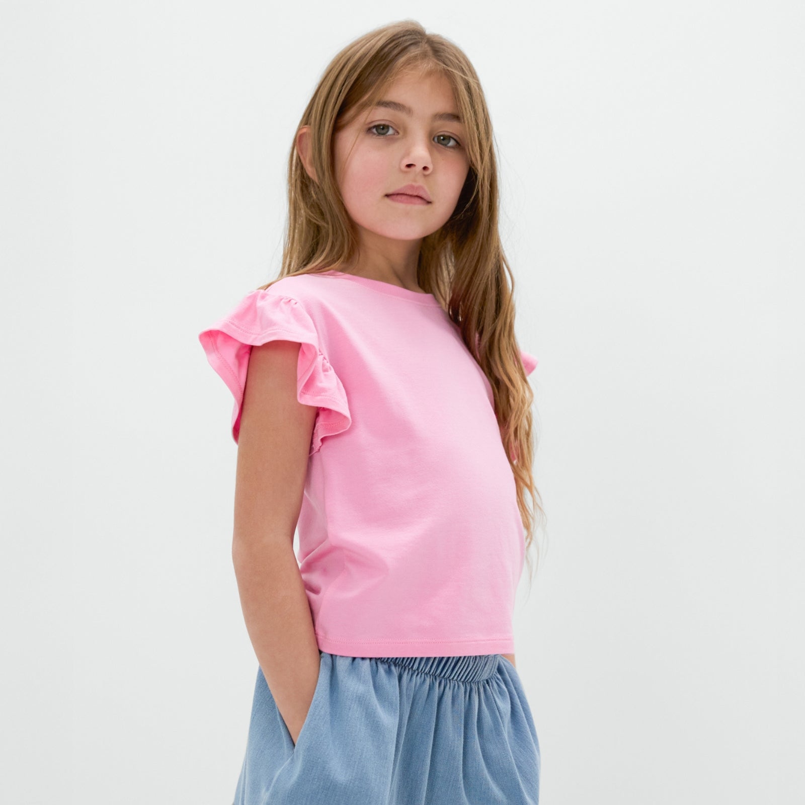 Standing child wearing the Light Blue Denim Skort with the Peppy Pink flutter tee