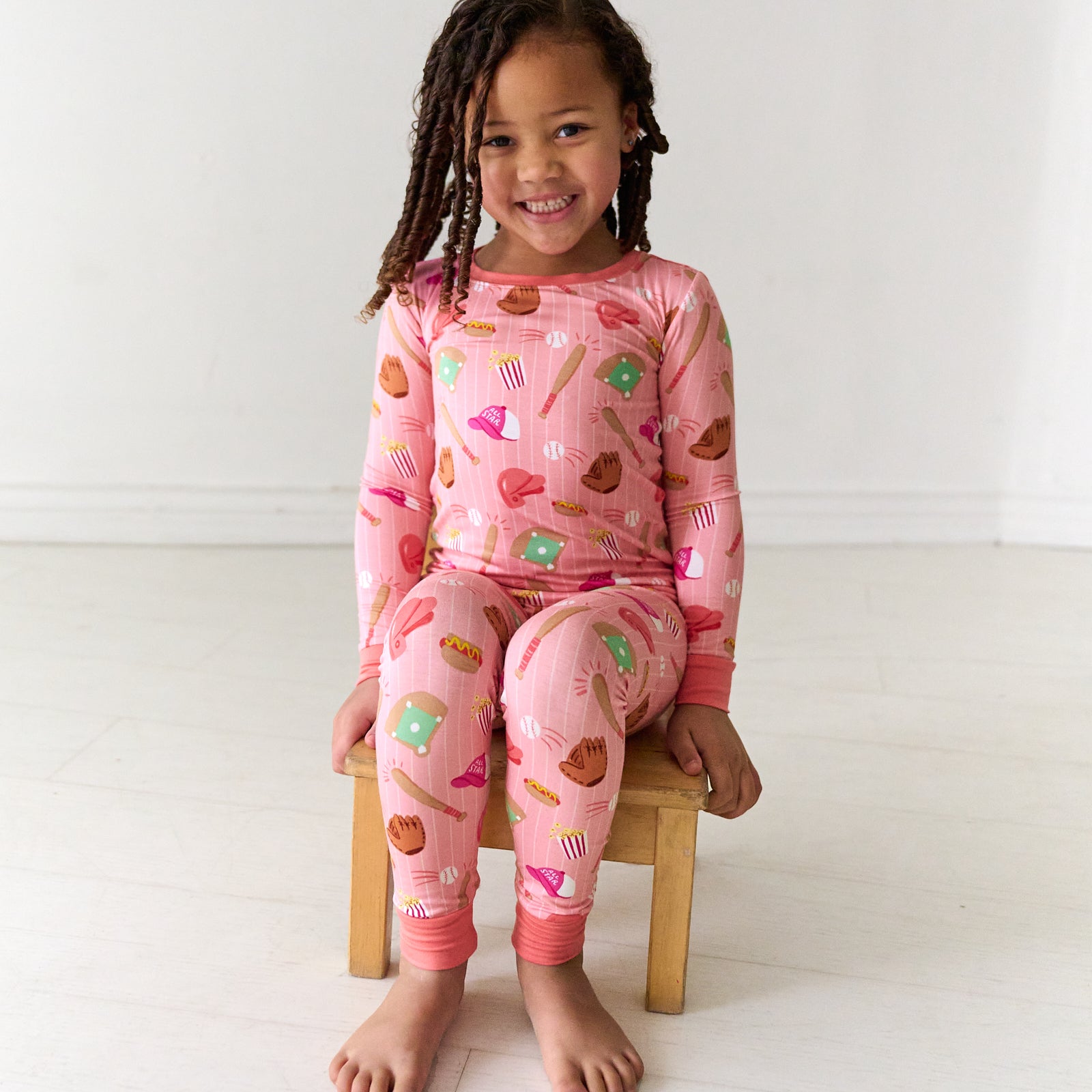 Child sitting on a stool wearing a Pink All Stars two-piece long sleeve and pants kids bamboo pajama set