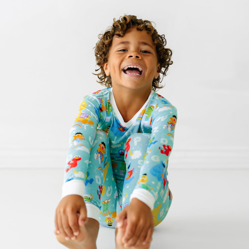 Child sitting on the ground laughing wearing a Spelling with Sesame Street two piece pajama set