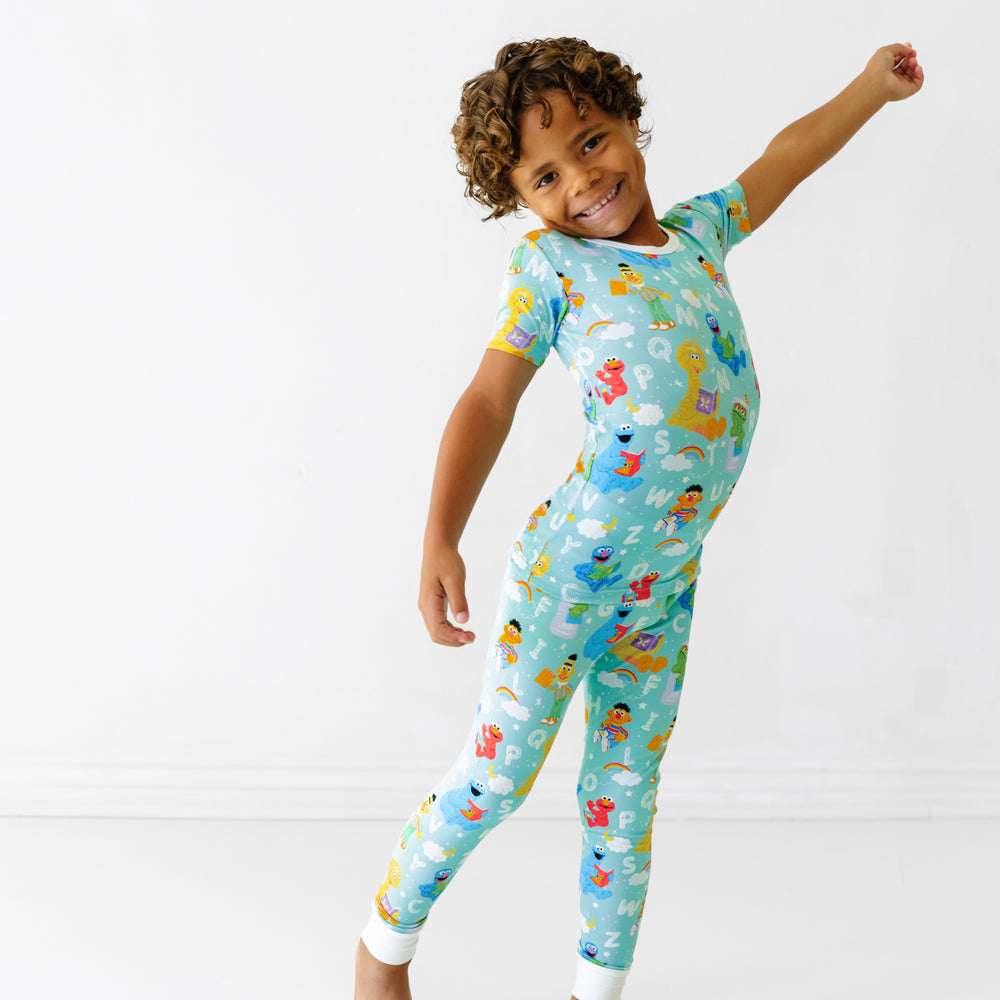 Child stretching wearing a Spelling with Sesame Street two piece short sleeve pajama set