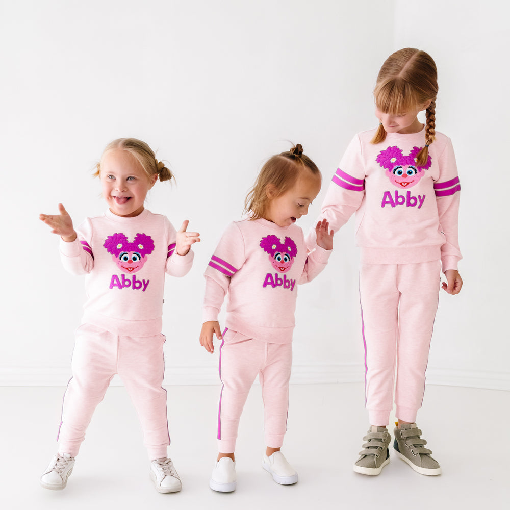 Three children wearing matching Sesame Street Abby crewneck sweatshirt and jogger sets