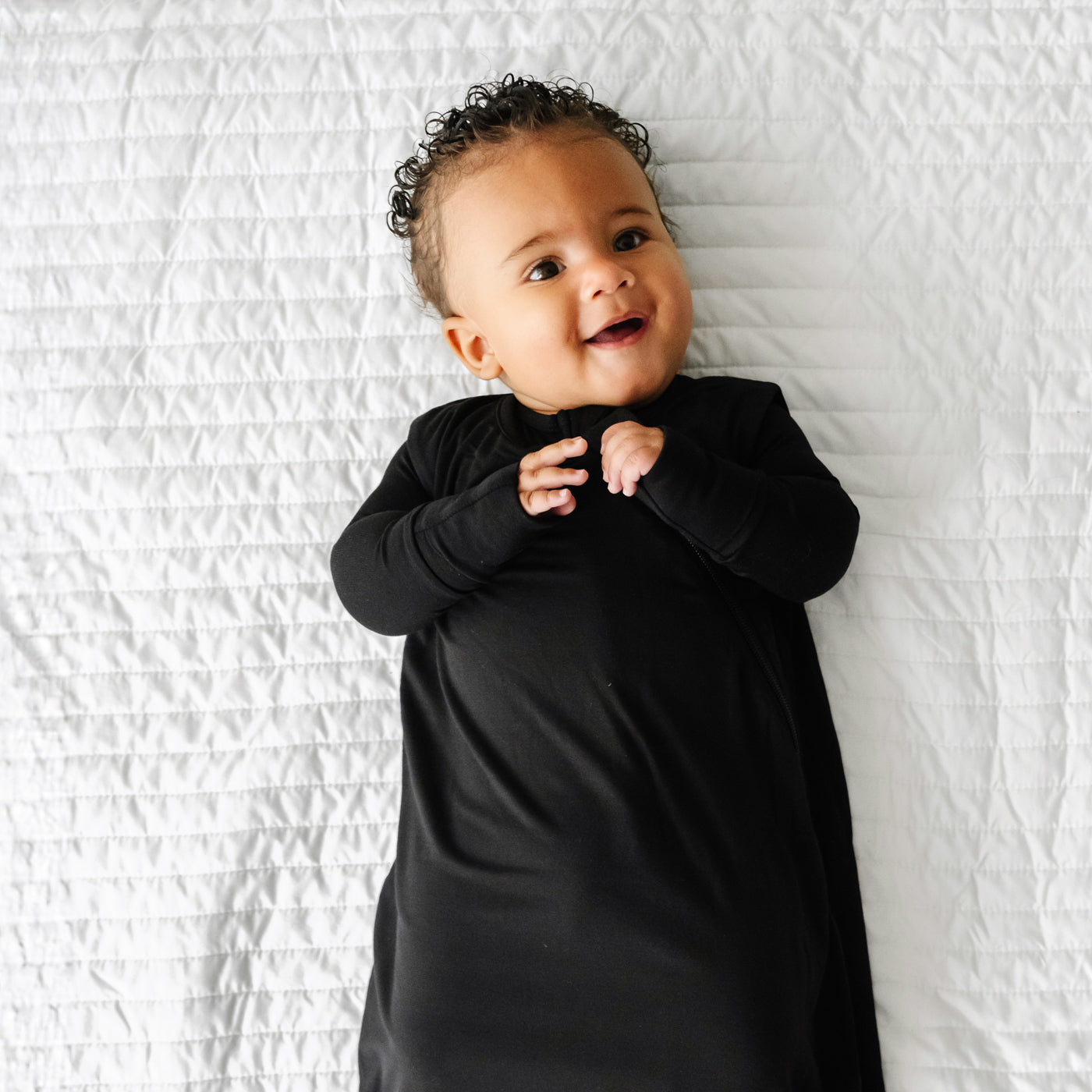 Close up image of a child laying on a blanket wearing a Black Sleepy Bag and matching zippy