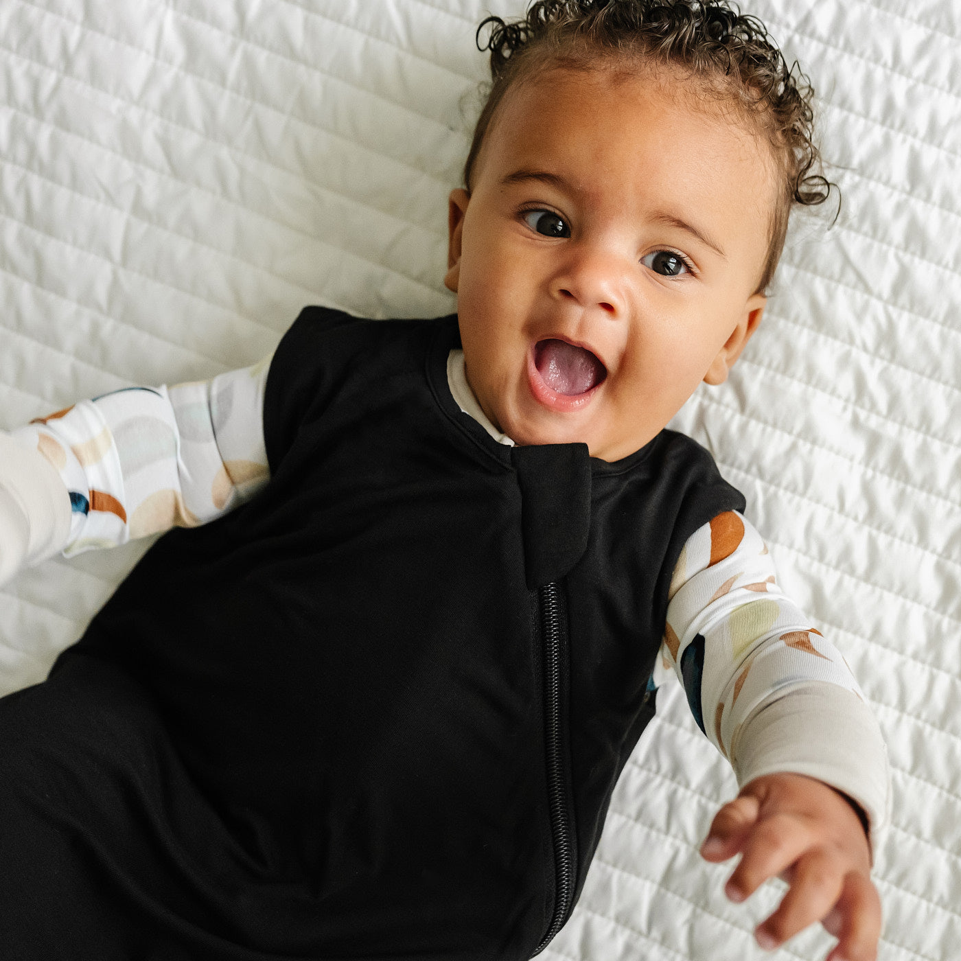 Alternate close up image of a child laying on a blanket wearing a Black Sleepy Bag and matching zippy