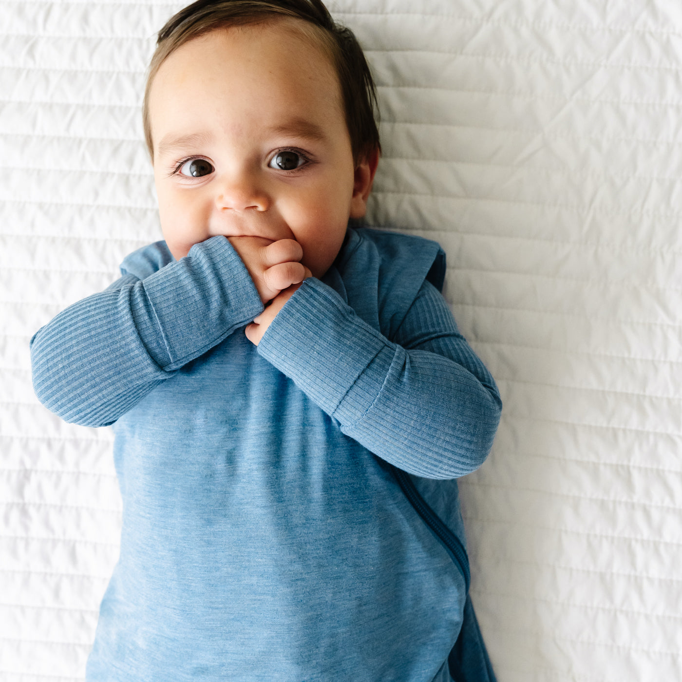 Close up image of a child laying on a blanket wearing a Heather Blue Sleepy Bag and matching zippy