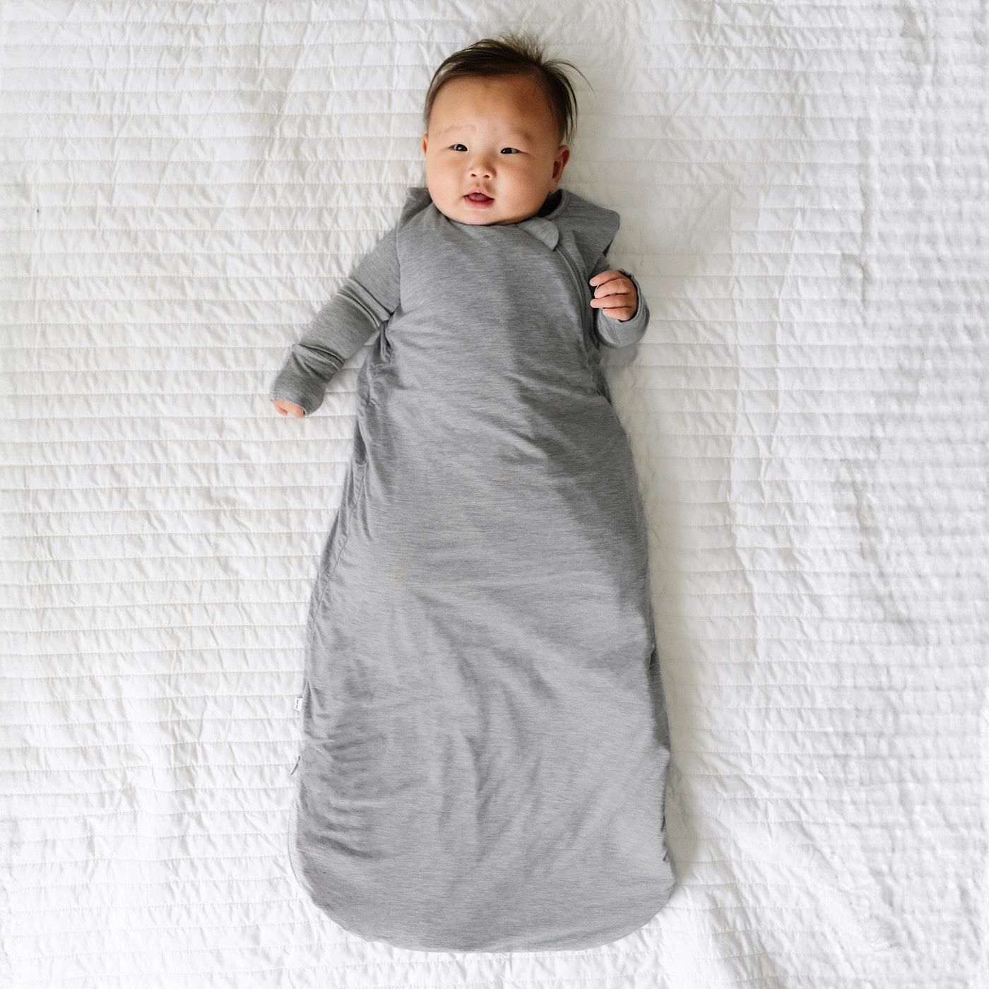 Child laying on a blanket wearing a Heather Gray Sleepy Bag and matching zippy