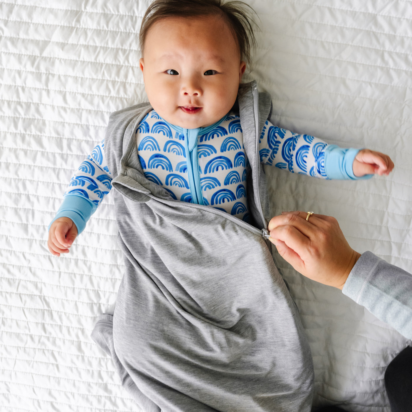 Child laying on a blanket wearing a Heather Gray Sleepy Bag with a parent zipping it up