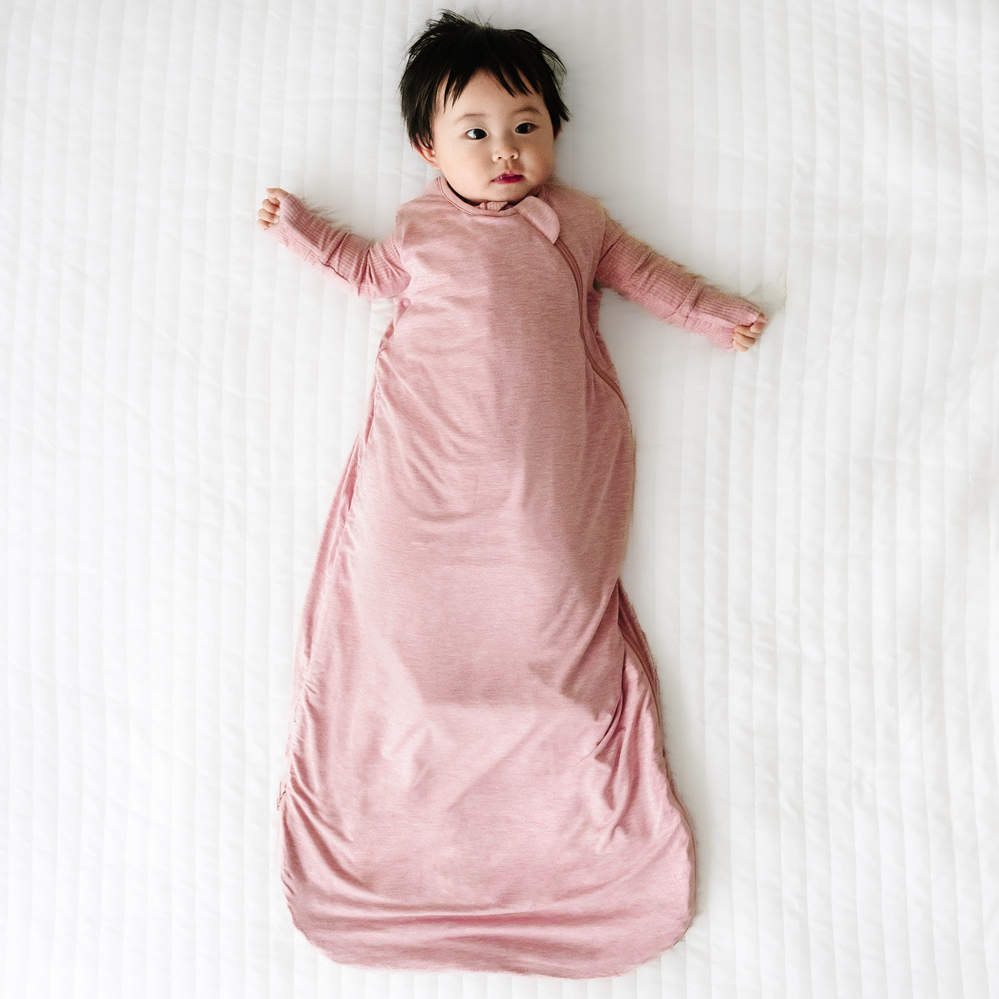Child laying on a blanket wearing a Heather Mauve sleepy bag and matching zippy