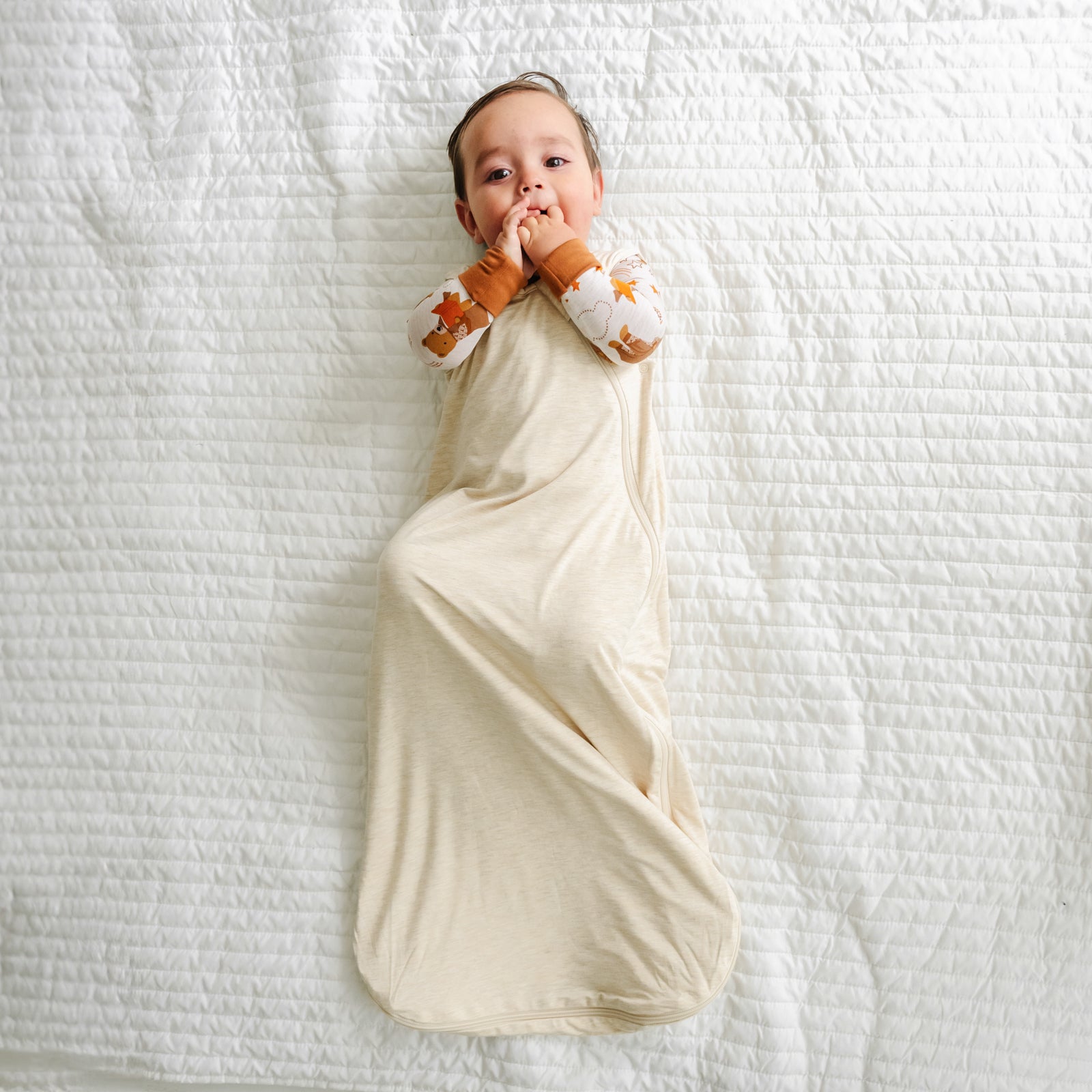 Child laying on a bed wearing a Beary Sleepy zippy in a Heather Oatmeal Sleepy bag