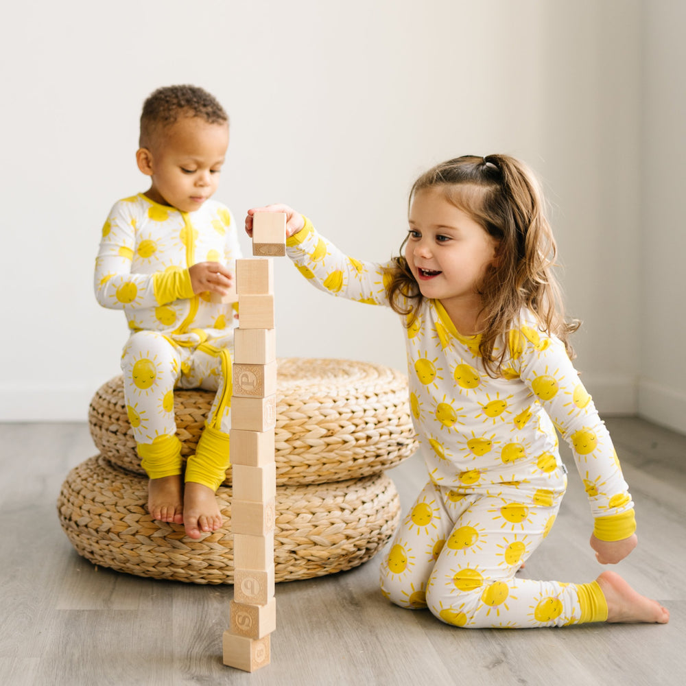 Image of two children playing with blocks and wearing two-piece pajama set with yellow smiling suns